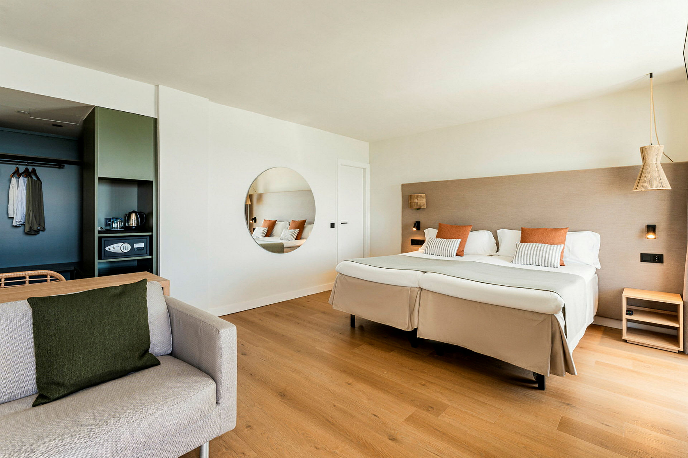 Et hotellrom med en stor dobbeltseng, et rundt speil på veggen og en sofa i forgrunnen. (AI-generert tekst)