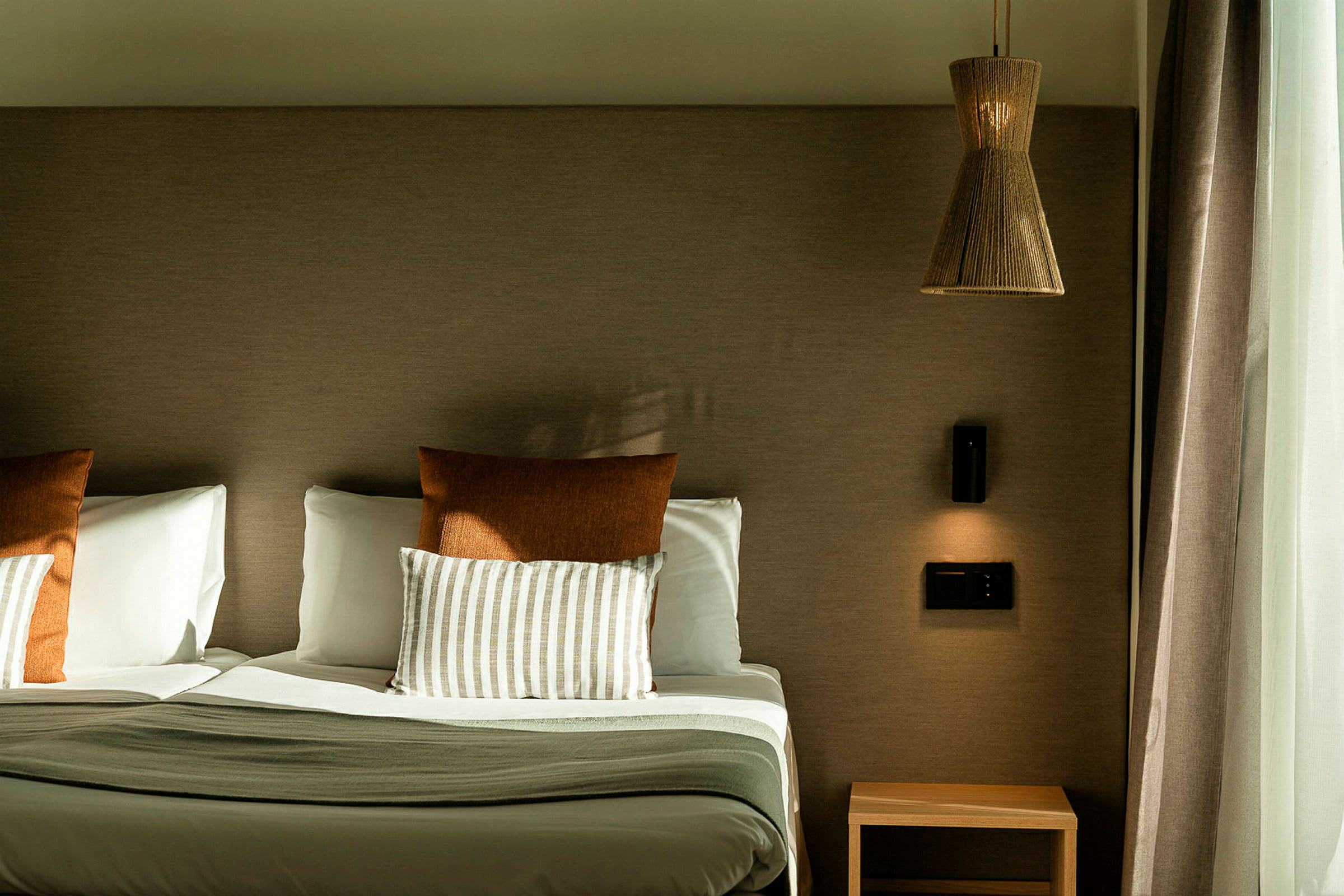 Hotellseng med to puter, et nattbord og en lampe på veggen. (AI-generert tekst)