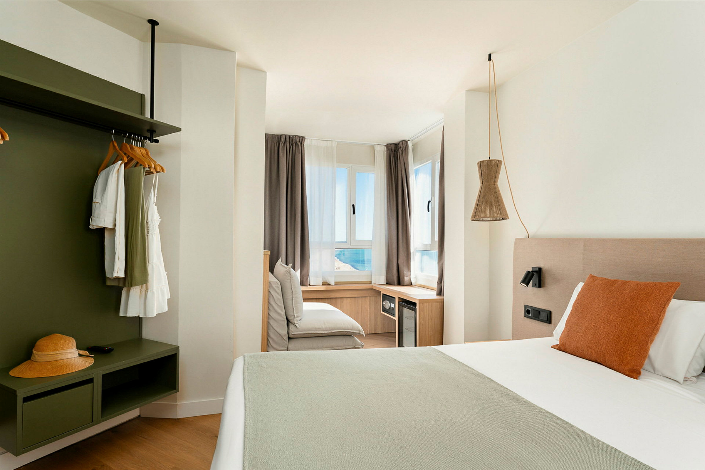 Et lyst og moderne hotellrom med en stor seng og utsikt til havet gjennom vinduene. (AI-generert tekst)