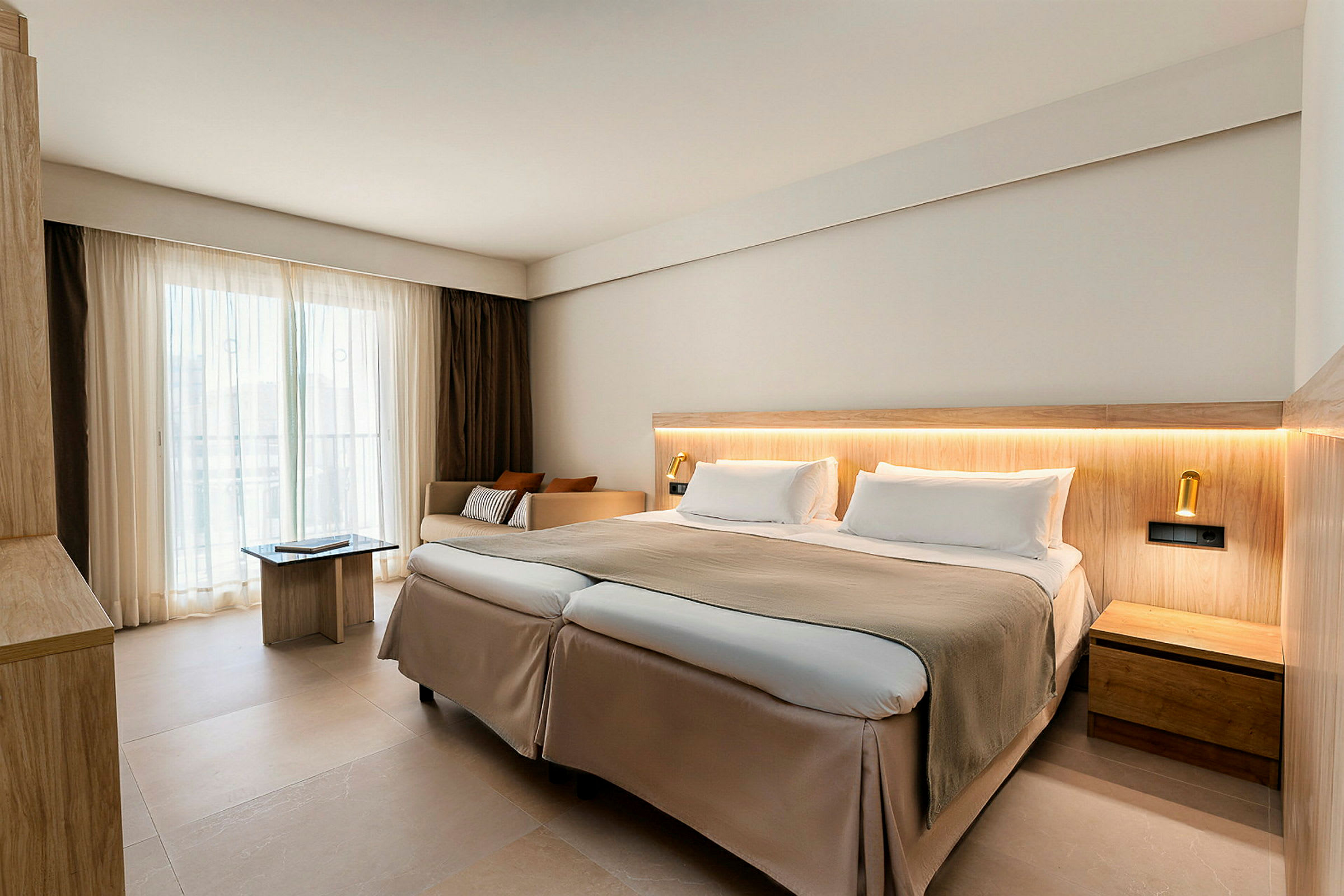 Et moderne hotellrom med en dobbeltseng, lyse farger og store vinduer med gardiner. (AI-generert tekst)
