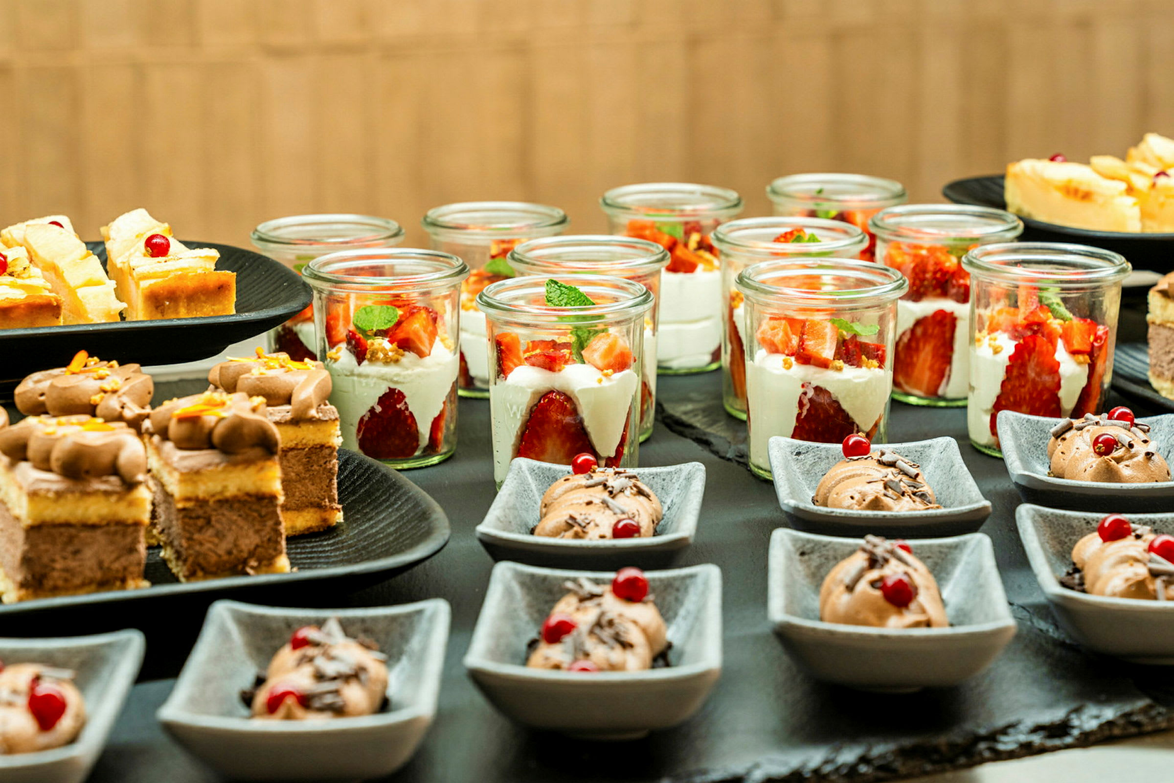 Et bord med forskjellige desserter, inkludert små glass med jordbær og krem og skåler med sjokolademousse. (AI-generert tekst)
