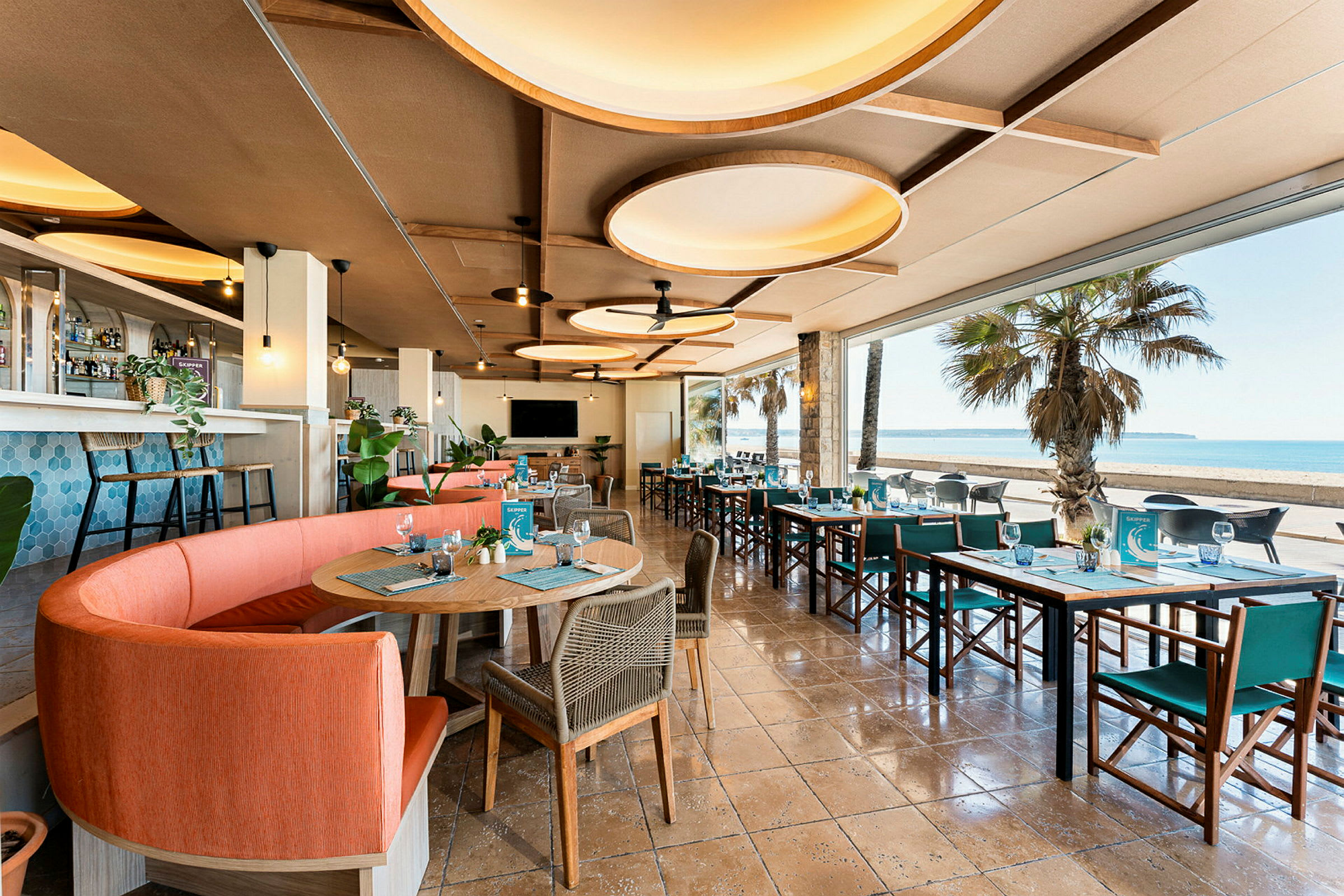 Restaurant med moderne møbler og store vinduer som vender mot en strand. (AI-generert tekst)