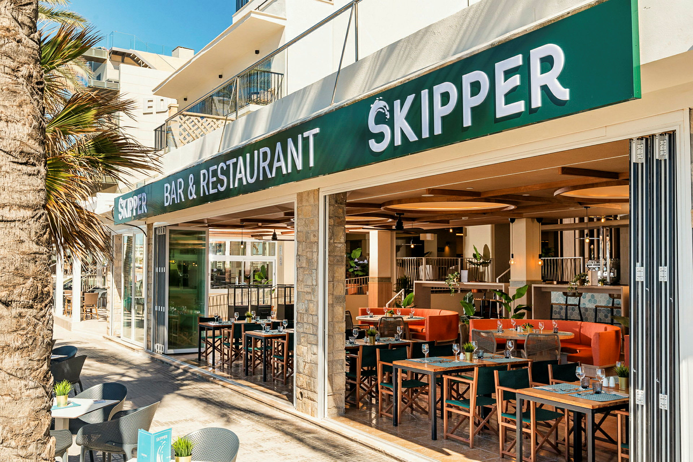 En restaurant og bar med navnet Skipper, utendørs sitteplasser og interiør synlig. (AI-generert tekst)