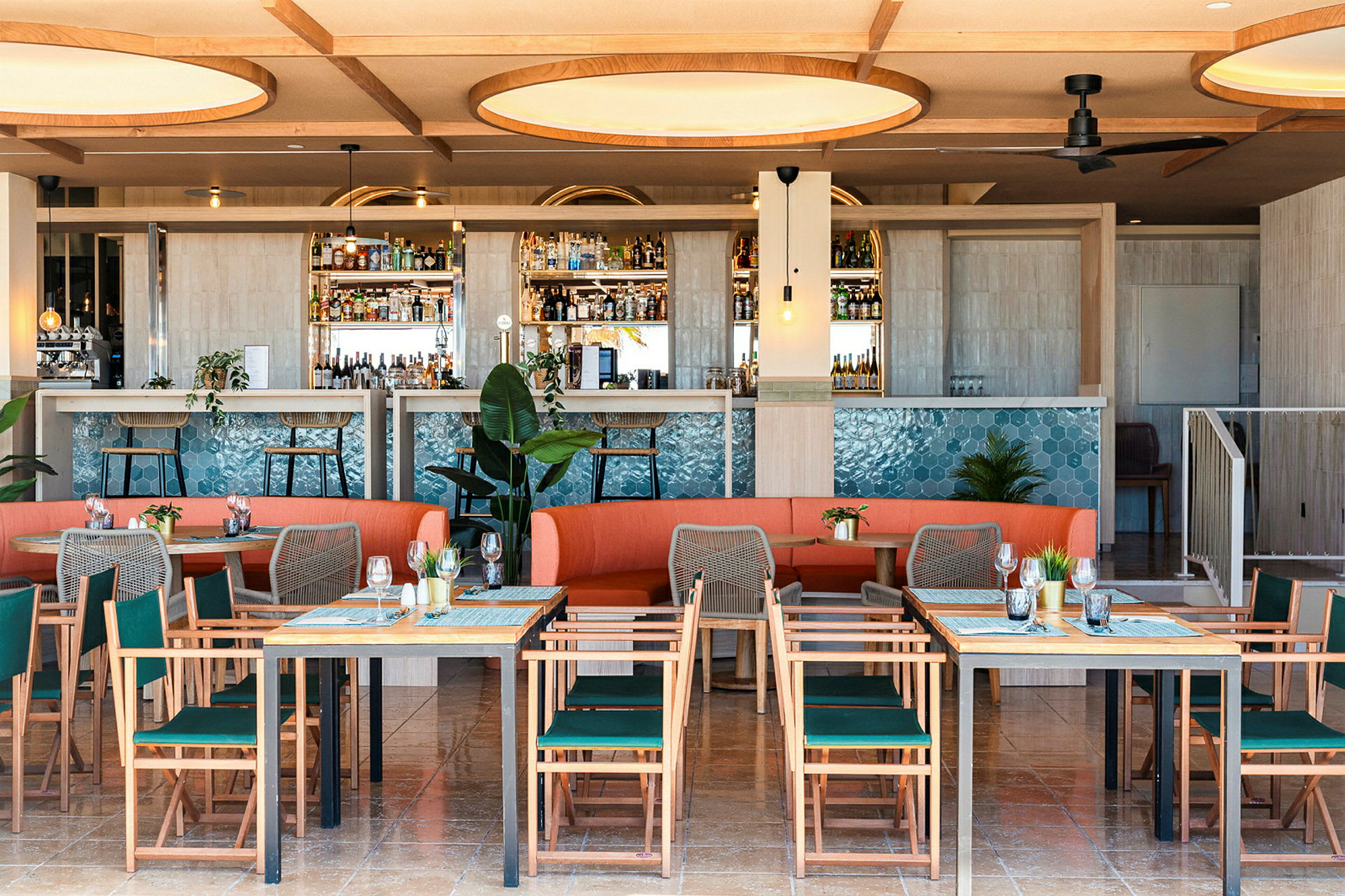 Bilde av en moderne restaurant med bord, stoler og en oransje sofa samt en barinnredning dekorert med blå fliser. (AI-generert tekst)