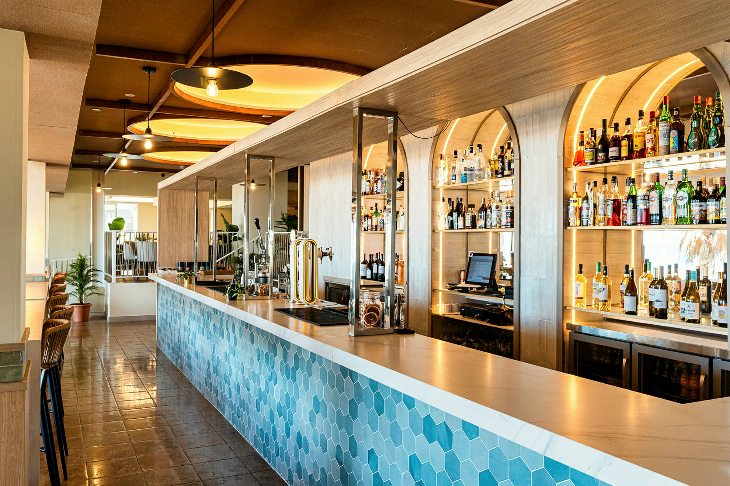 En moderne bar med en blå sekskantmønstret bardisk og hyller fylt med flasker og drikker i bakgrunnen. (AI-generert tekst)