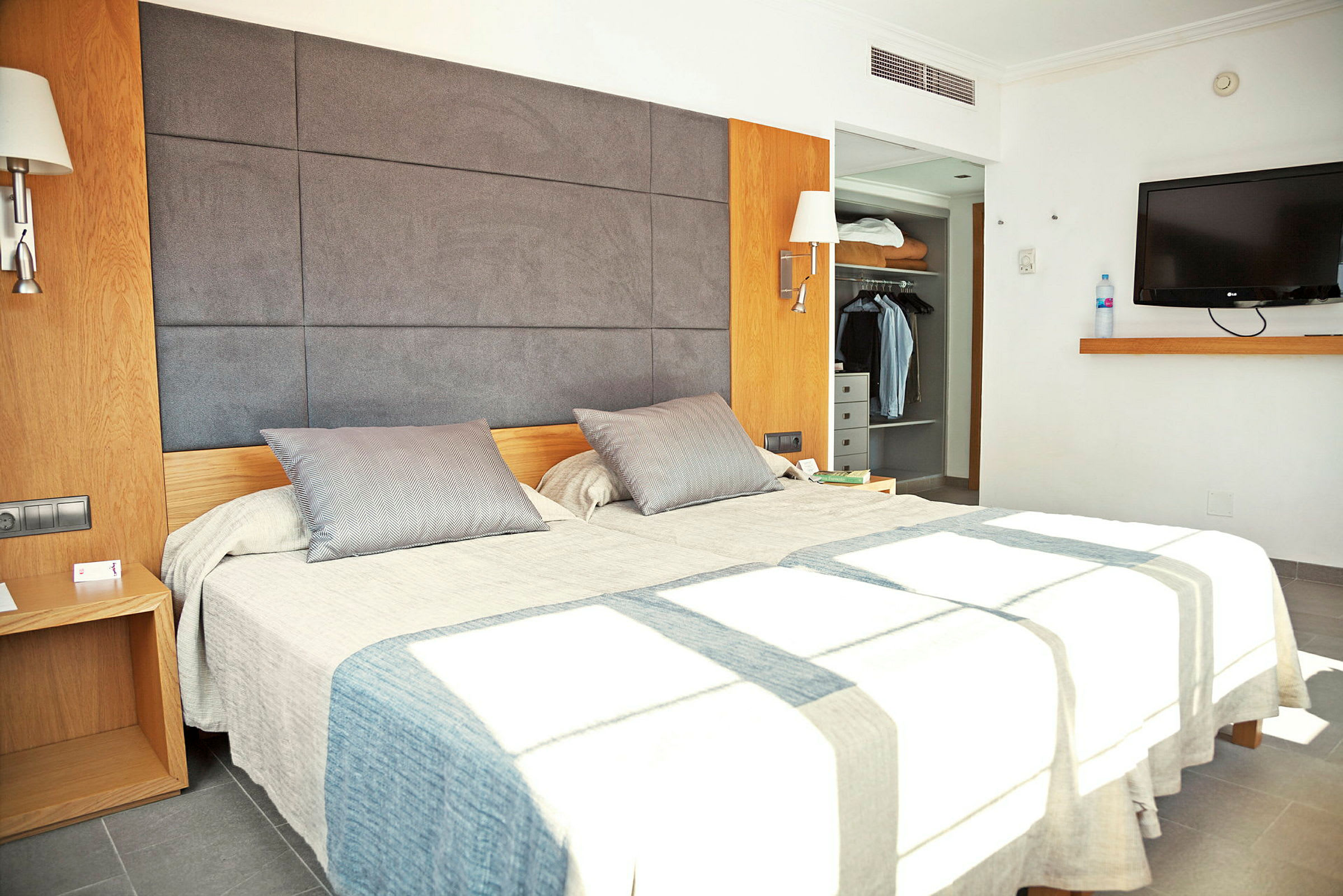 Bilde som viser et moderne hotellrom med en dobbeltseng, et garderobeskap og en veggmontert TV. (AI-generert tekst)