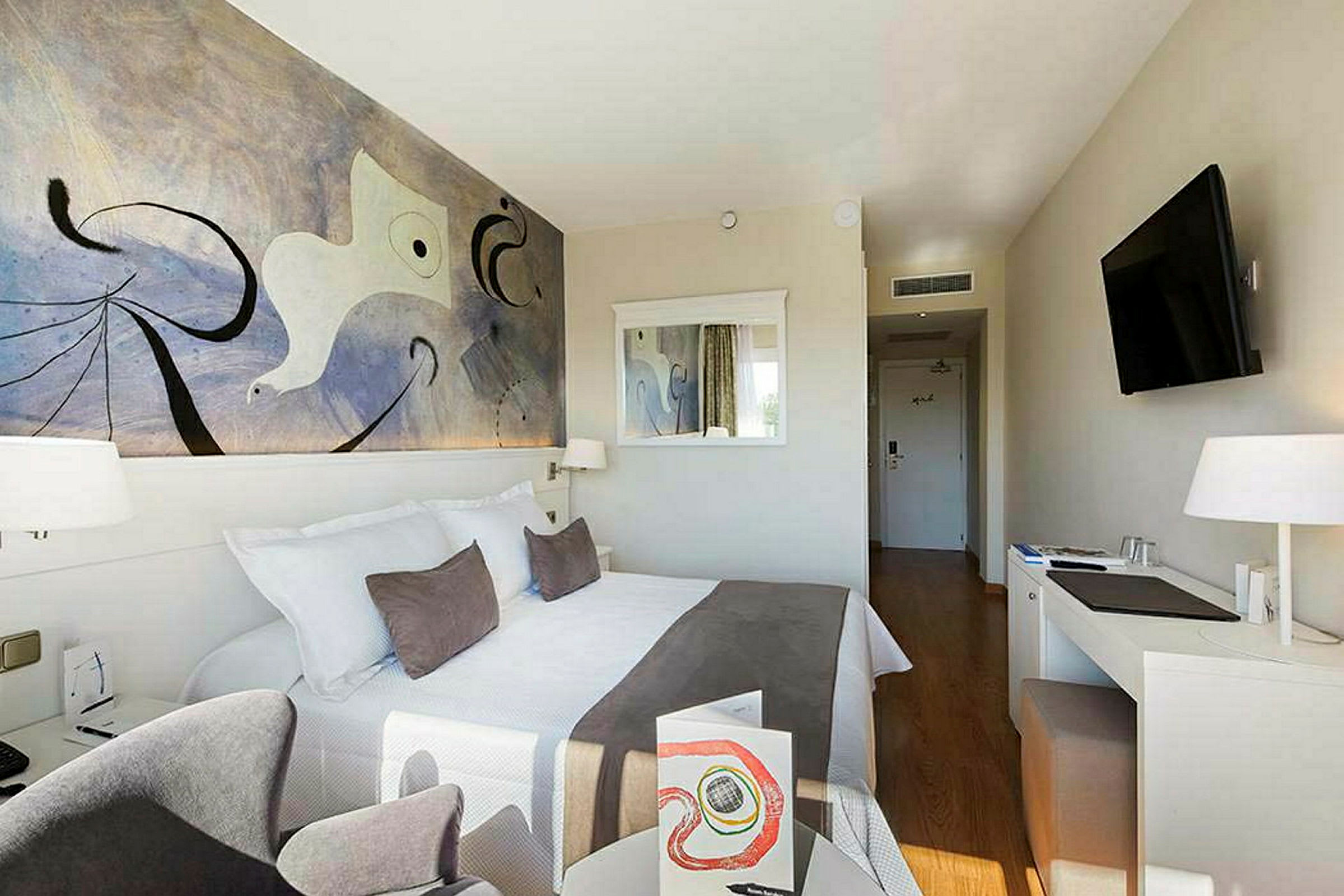 Et hotellrom med en dobbeltseng, veggkunst, speil, skrivebord og en TV. (AI-generert tekst)