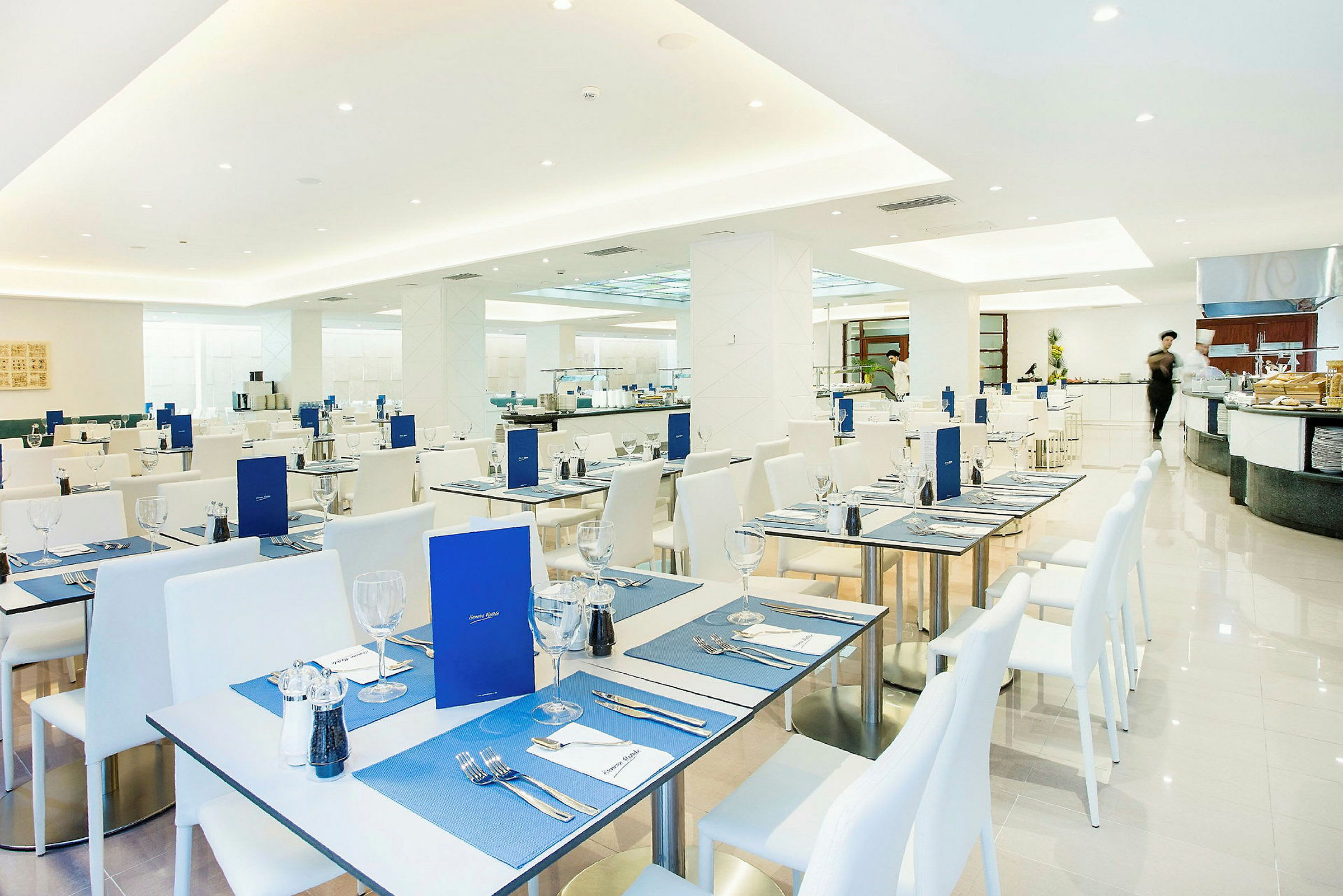 Restaurant med hvite bord og stoler, dekket med blå bordbrikker og menyer. (AI-generert tekst)