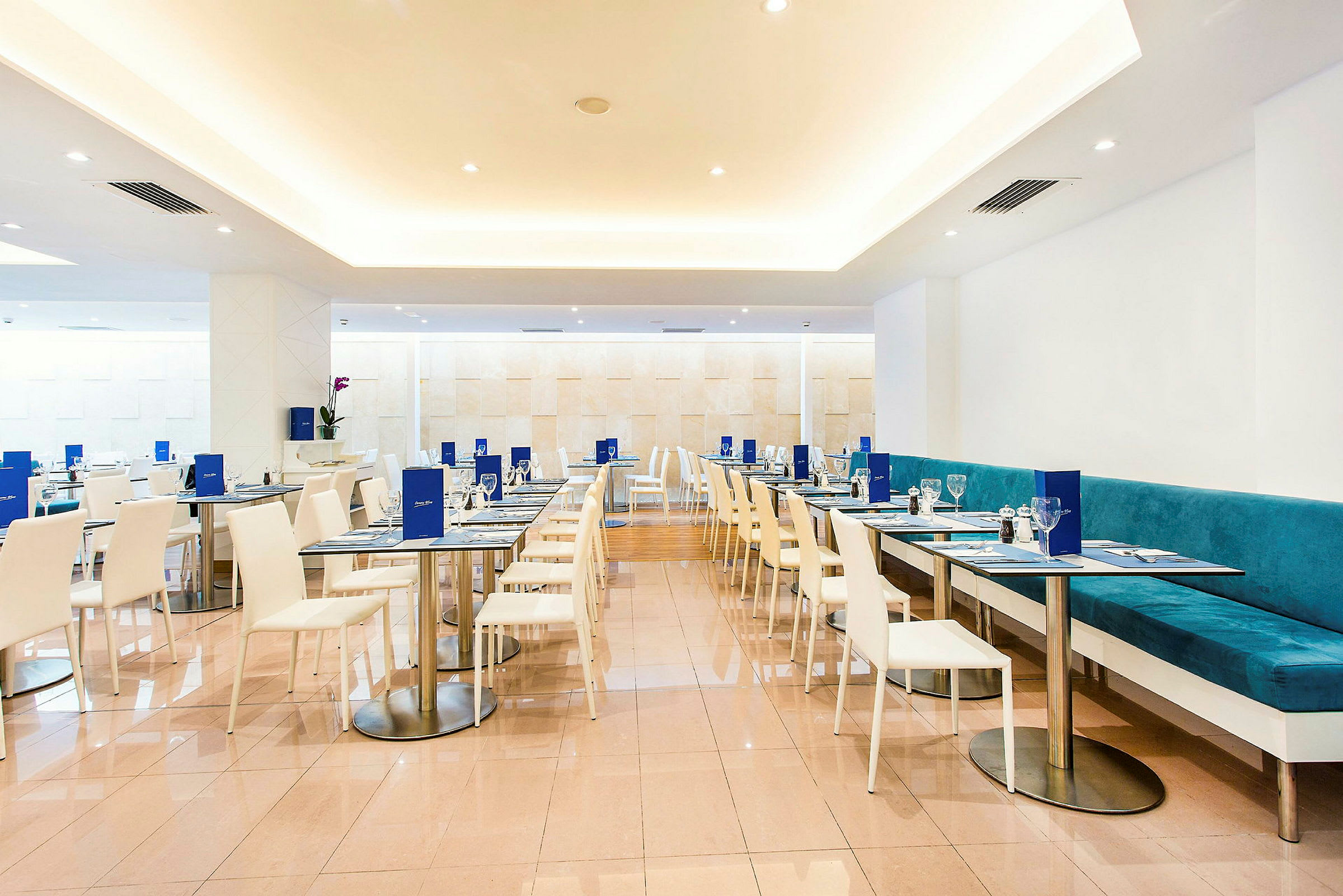 Interiør av en moderne restaurant med hvite stoler og bord samt turkise sofaer. (AI-generert tekst)