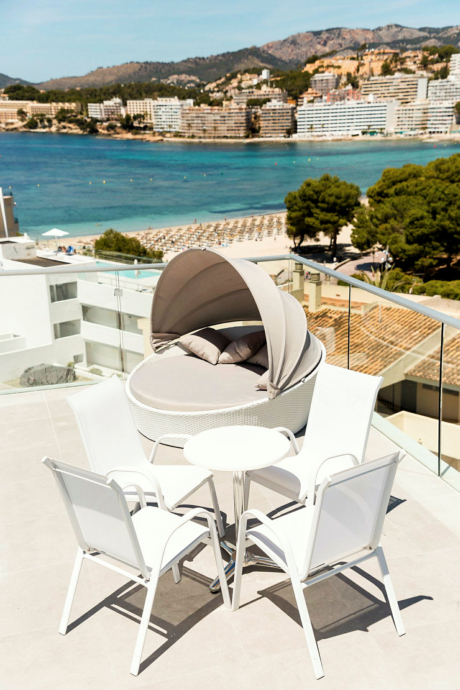 Terrasse med hvitt sittemøblement og solseng på en moderne ferieanlegg med utsikt over stranden og havet. (AI-generert tekst)