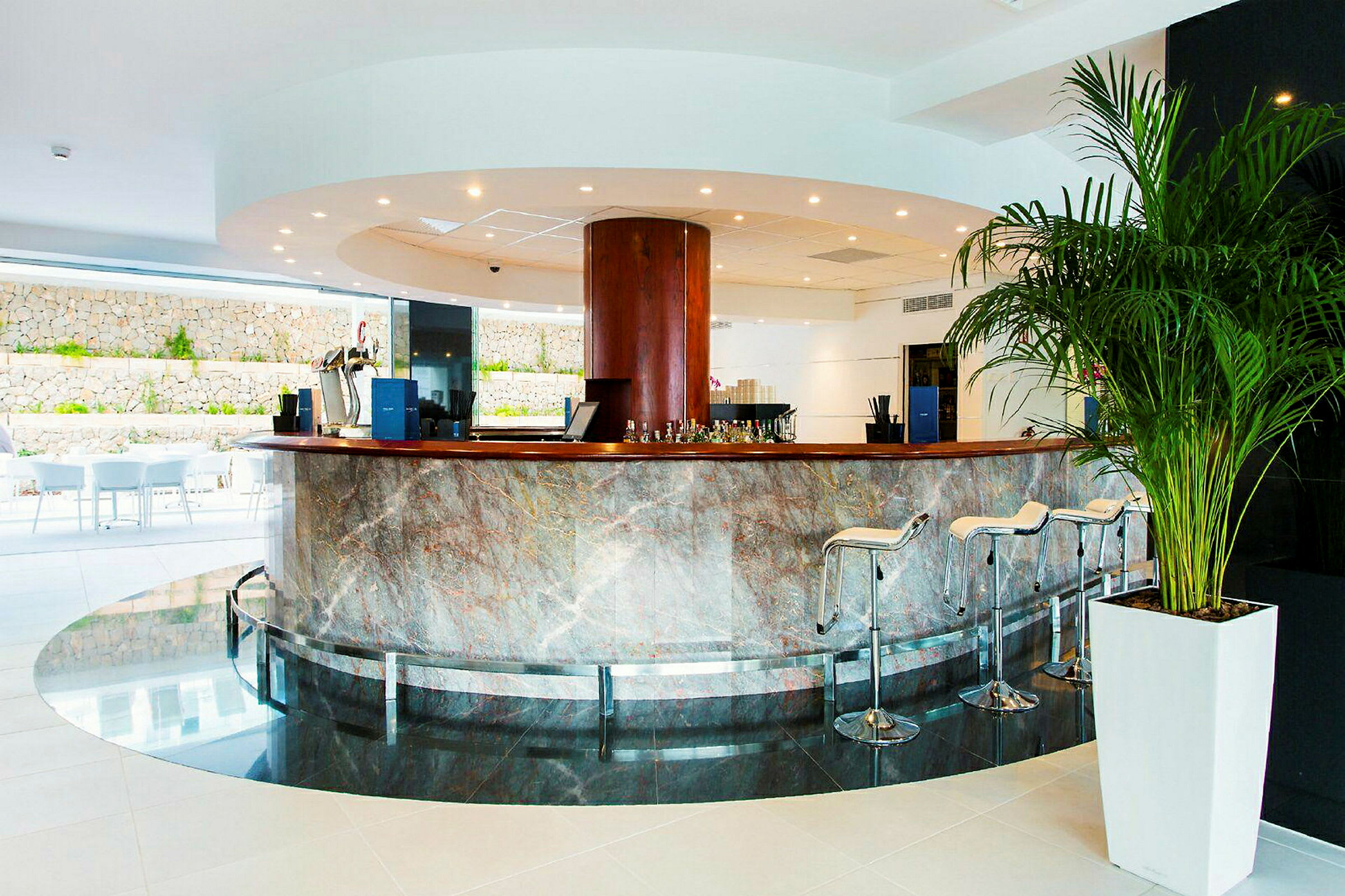 En moderne hotellobby med en sentralt plassert rund disk, omgitt av høye stoler og dekorert med polert stein. (AI-generert tekst)