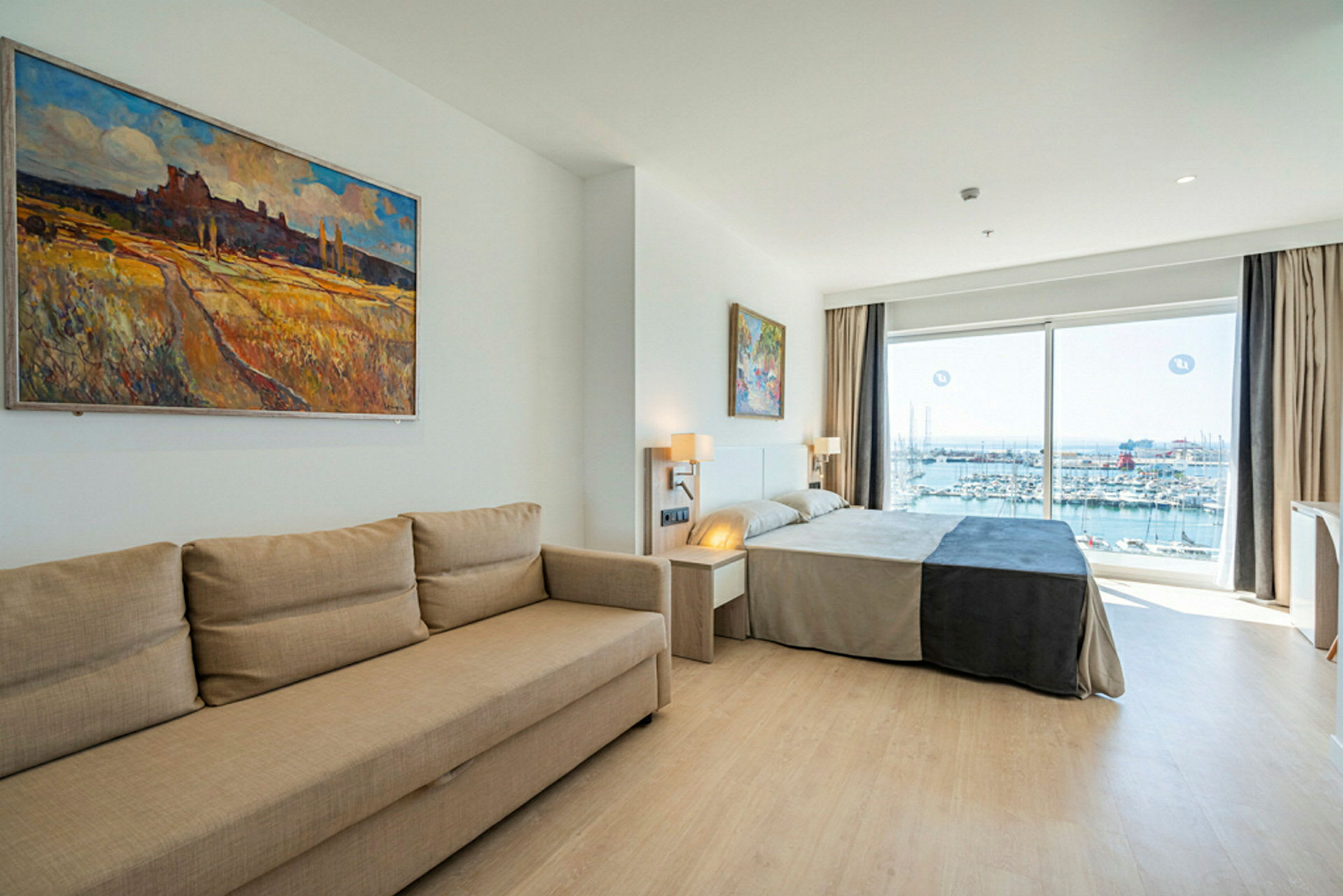 Et hotellrom med en sofa, en seng og vinduer som viser utsikt over en marina. (AI-generert tekst)