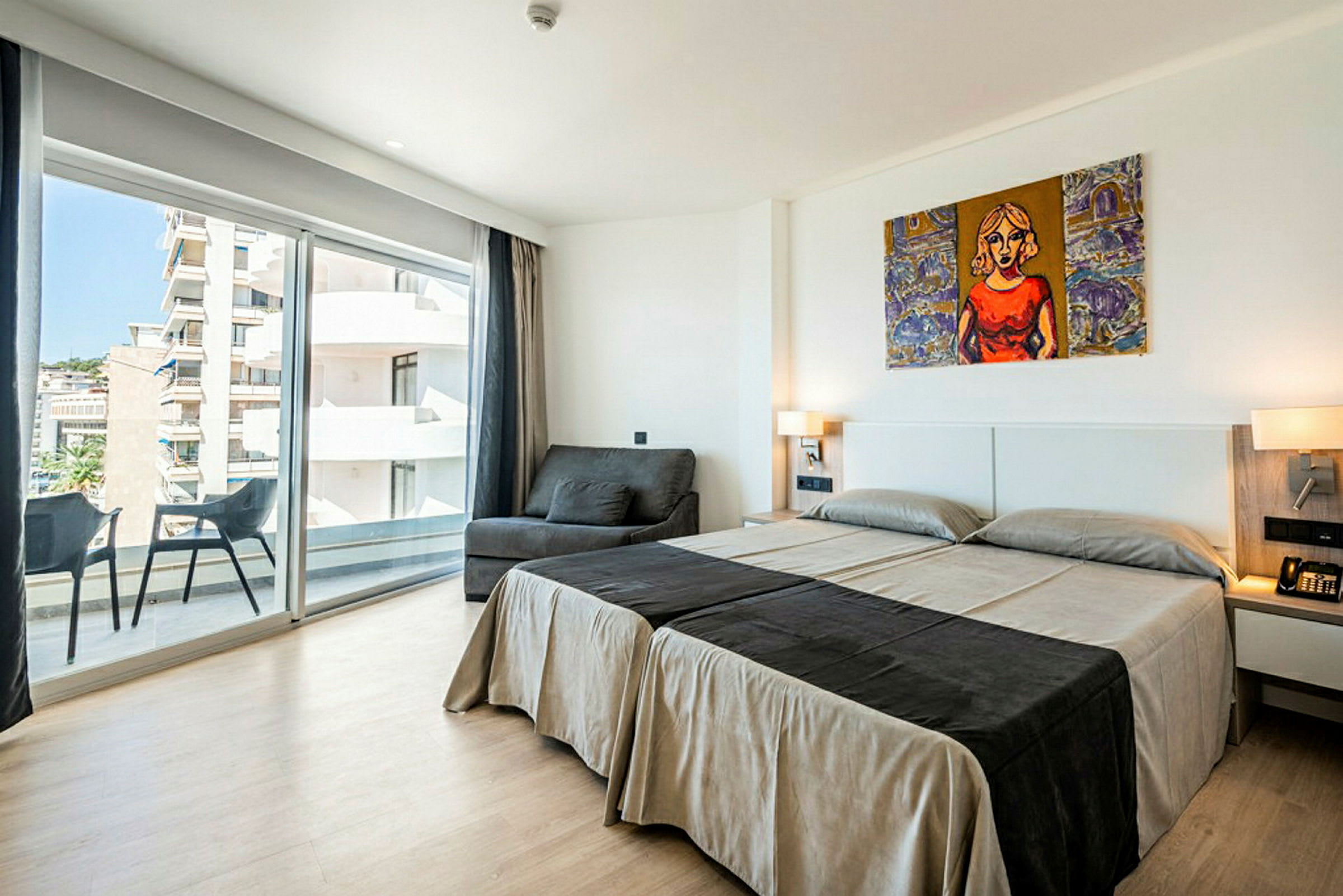 Et hotellrom med to enkeltsenger, en sofa, en balkong og store glassvinduer. (AI-generert tekst)