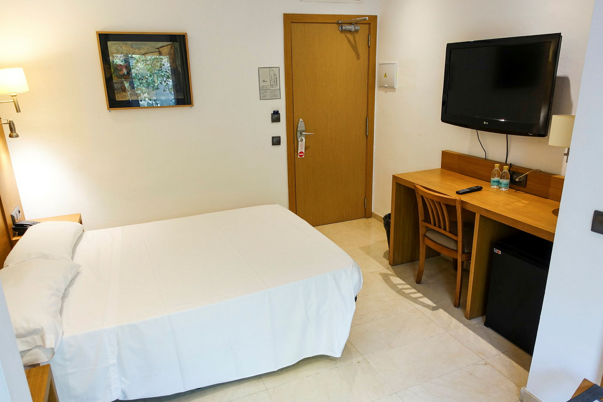 Et enkelt hotellrom med en seng, skrivebord og stol. På veggen er det en TV og et kunstverk. (AI-generert tekst)
