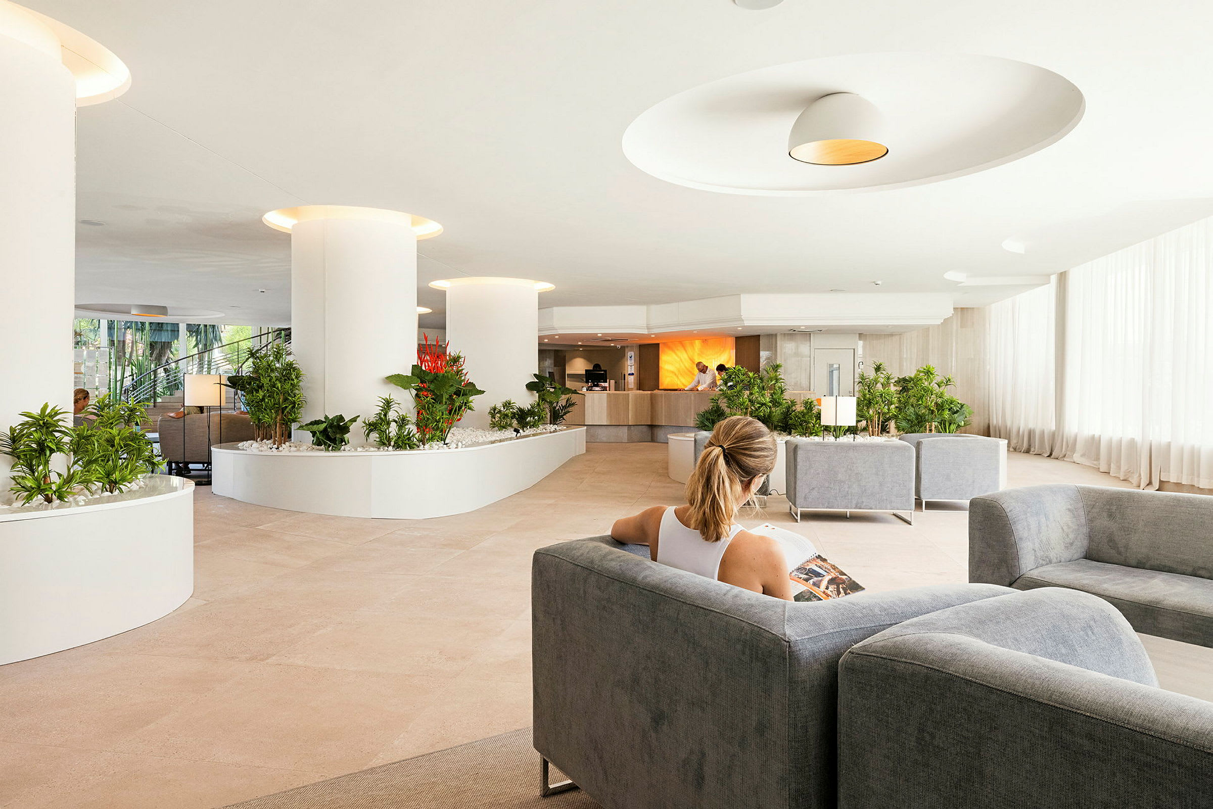 Person sitter i en romslig hotellobby med moderne innredning og grønnplanter. (AI-generert tekst)
