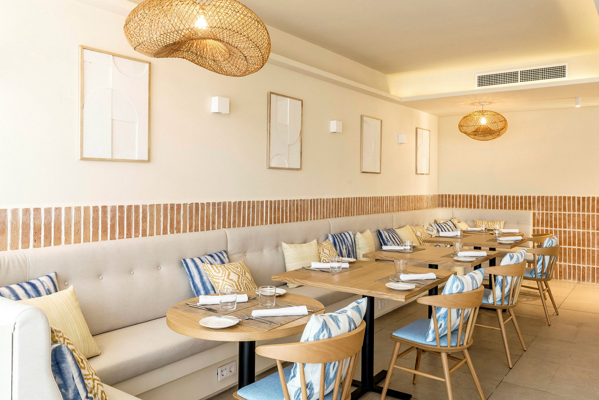 En restaurant med trebord, stoler og beige sittebenker dekorert med fargerike puter. (AI-generert tekst)