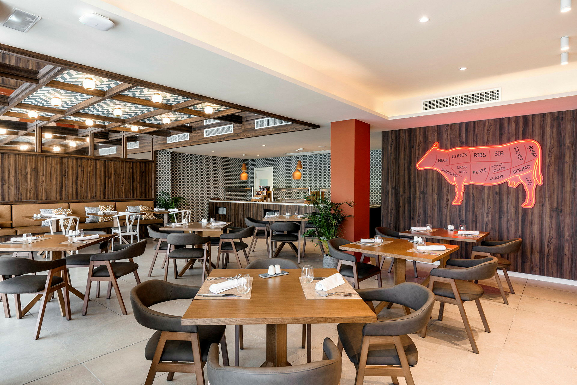 Interiør av en restaurant med flere trebord og stoler, veggdekorasjon i form av et neonskilt av en ku. (AI-generert tekst)