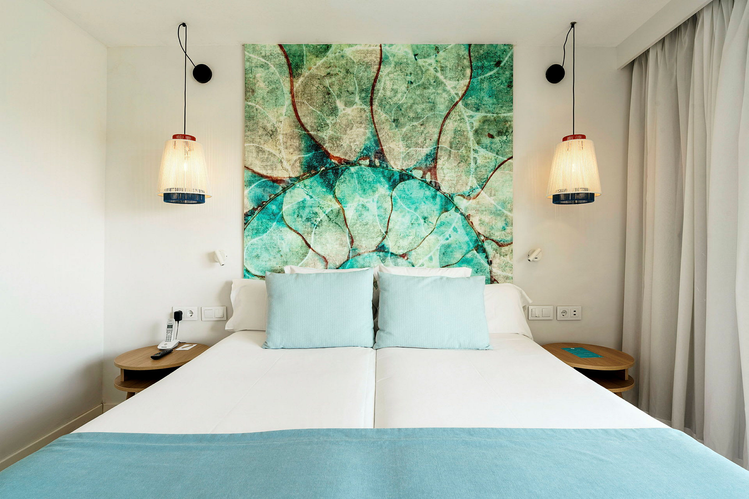 Hotellseng med turkise puter og en sengegavl med naturmotiv. (AI-generert tekst)