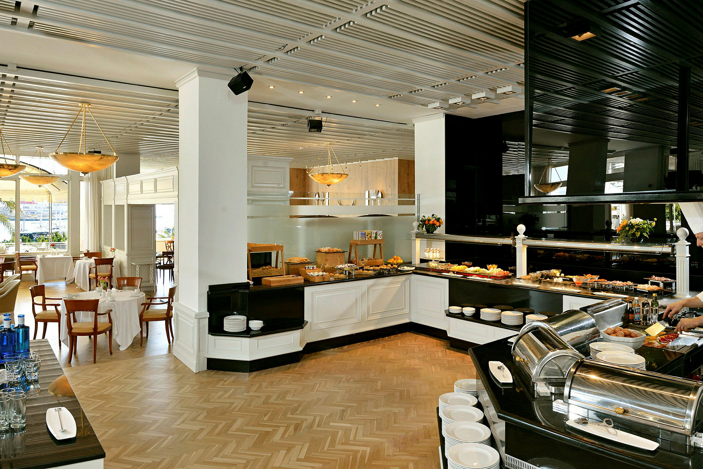 Innredning av en spisesal med frokostbuffet, bord med duker og stoler, samt flere serveringsområder. (AI-generert tekst)