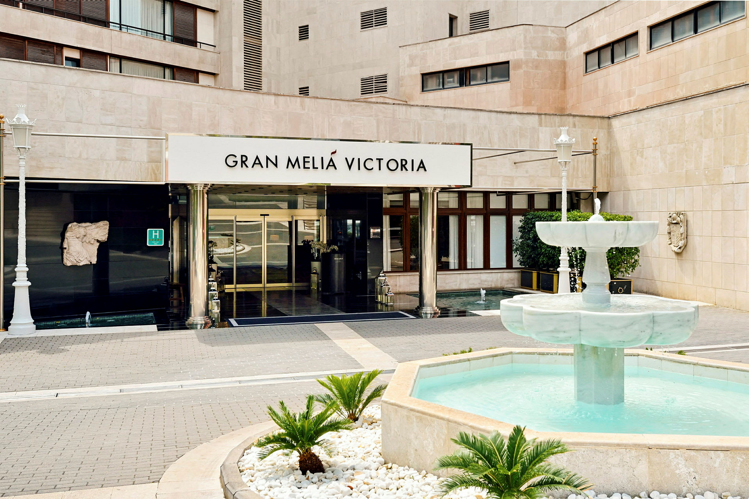 Inngangen til en bygning med teksten "Gran Meliá Victoria" over dørene og en fontene med klart vann foran. (AI-generert tekst)