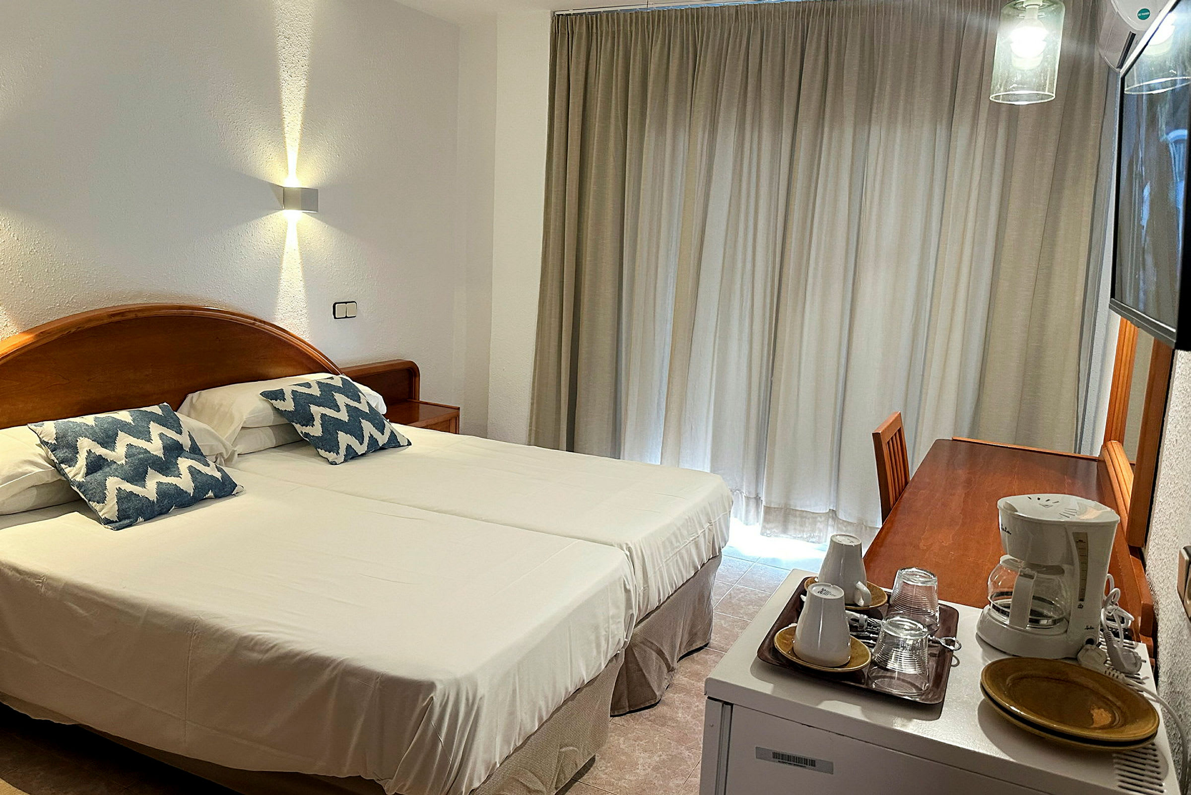 Et hotellrom med to enkeltsenger, et skrivebord og en kaffemaskin. (AI-generert tekst)