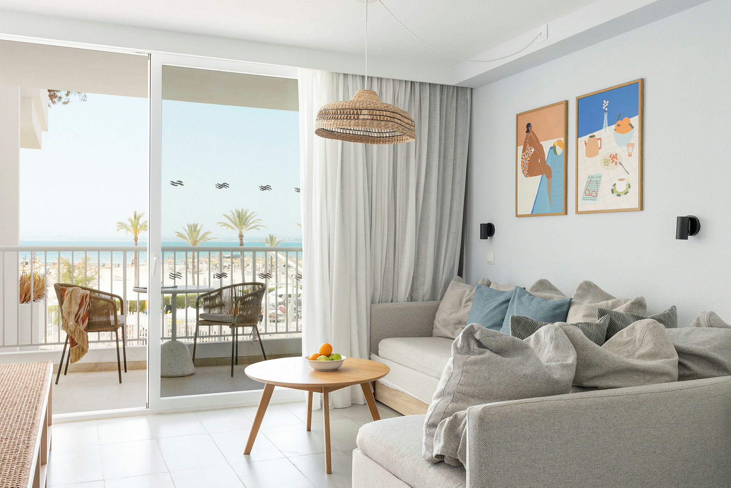Et lyst og moderne hotellrom med en sofa, sofabord og dører som åpner seg mot en balkong med havutsikt. (AI-generert tekst)