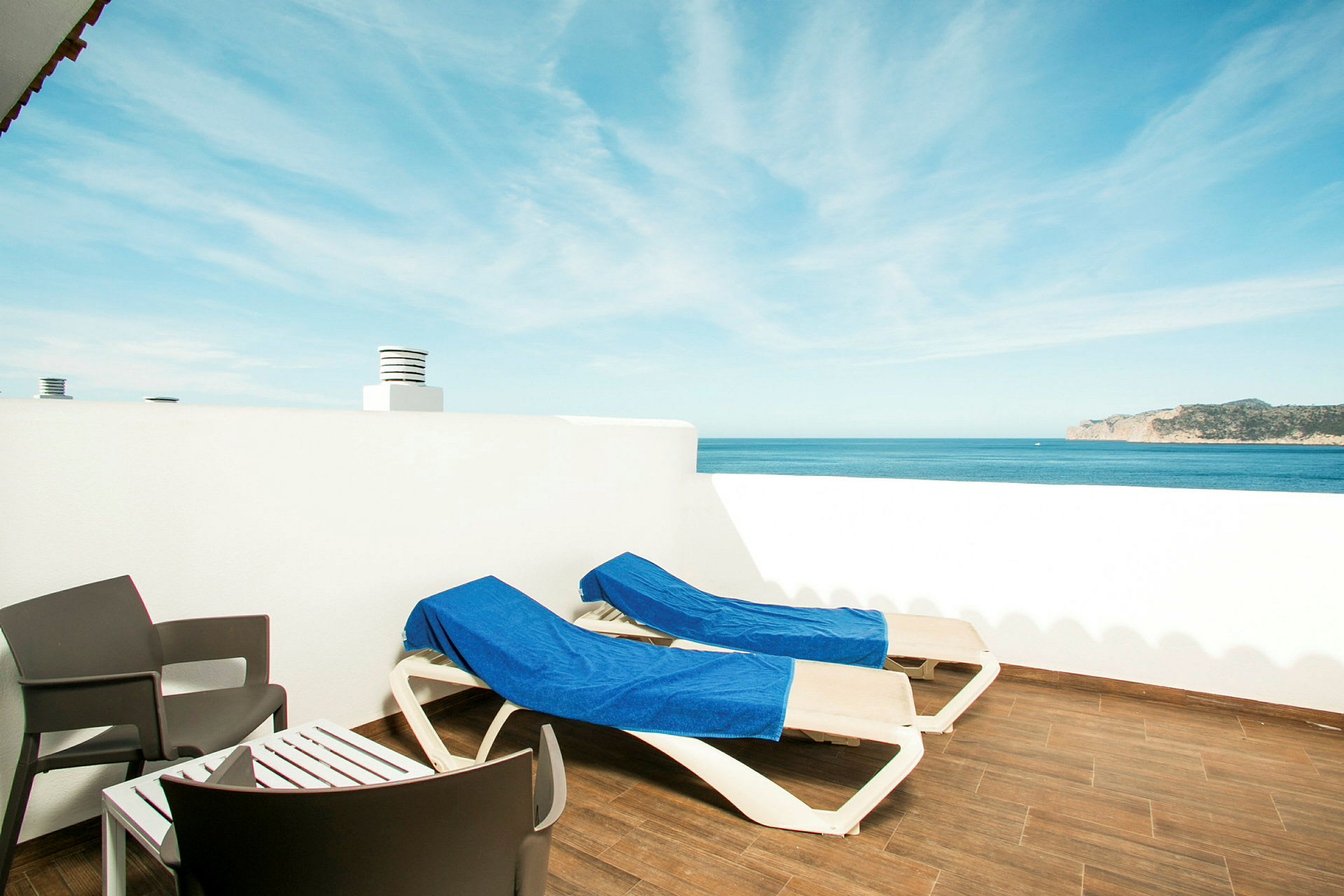To solsenger med blå håndklær på en terrasse med utsikt over havet. (AI-generert tekst)