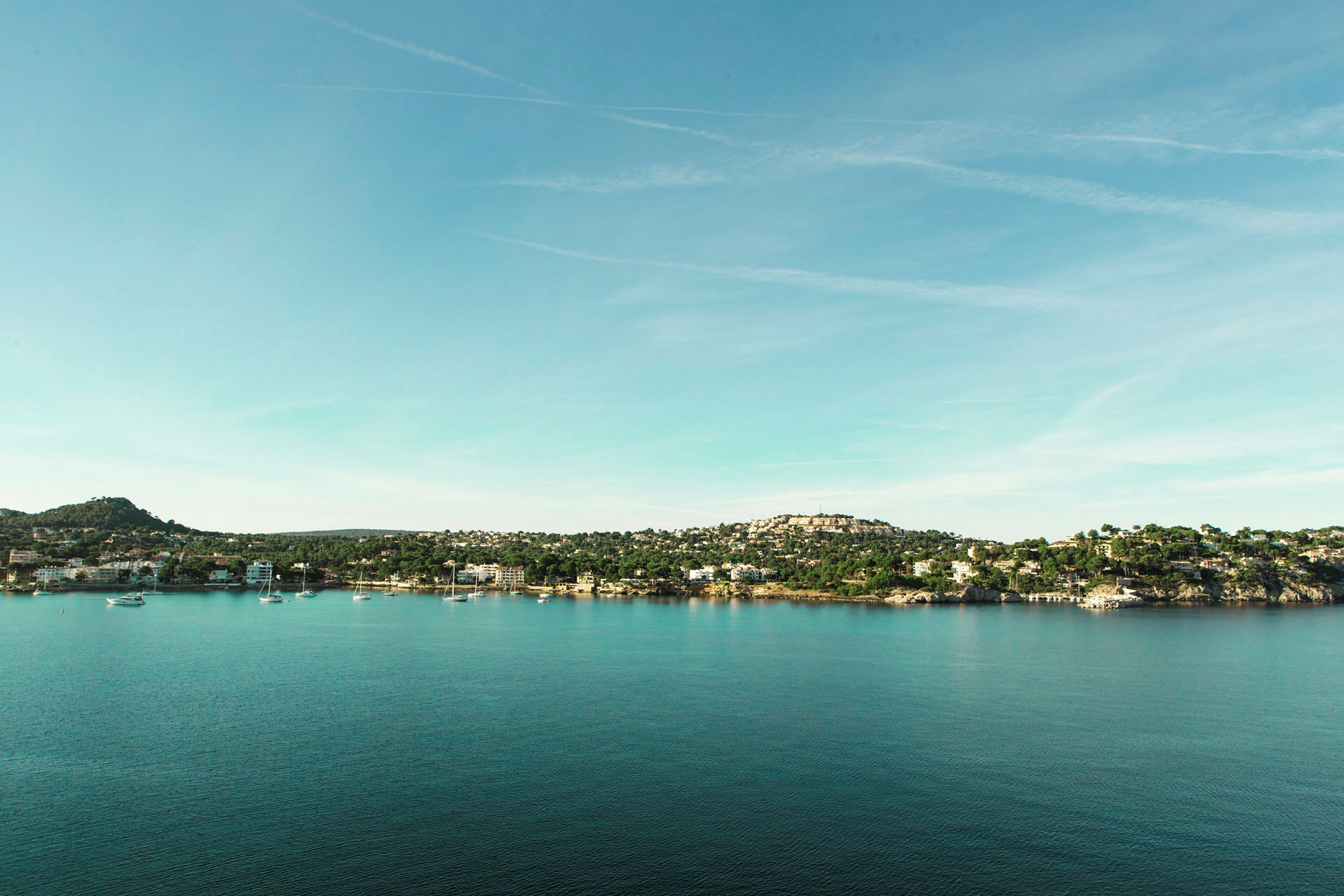 Utsikt over en kystlinje med hus og båter ved vannet under en klar himmel. (AI-generert tekst)