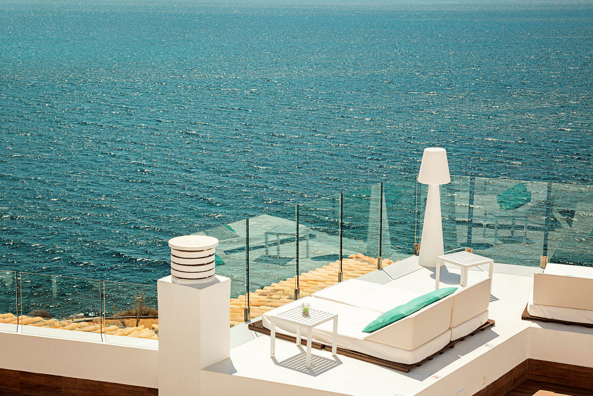 Utsikt over havet fra en terrasse med hvite møbler og glassrekkverk. (AI-generert tekst)