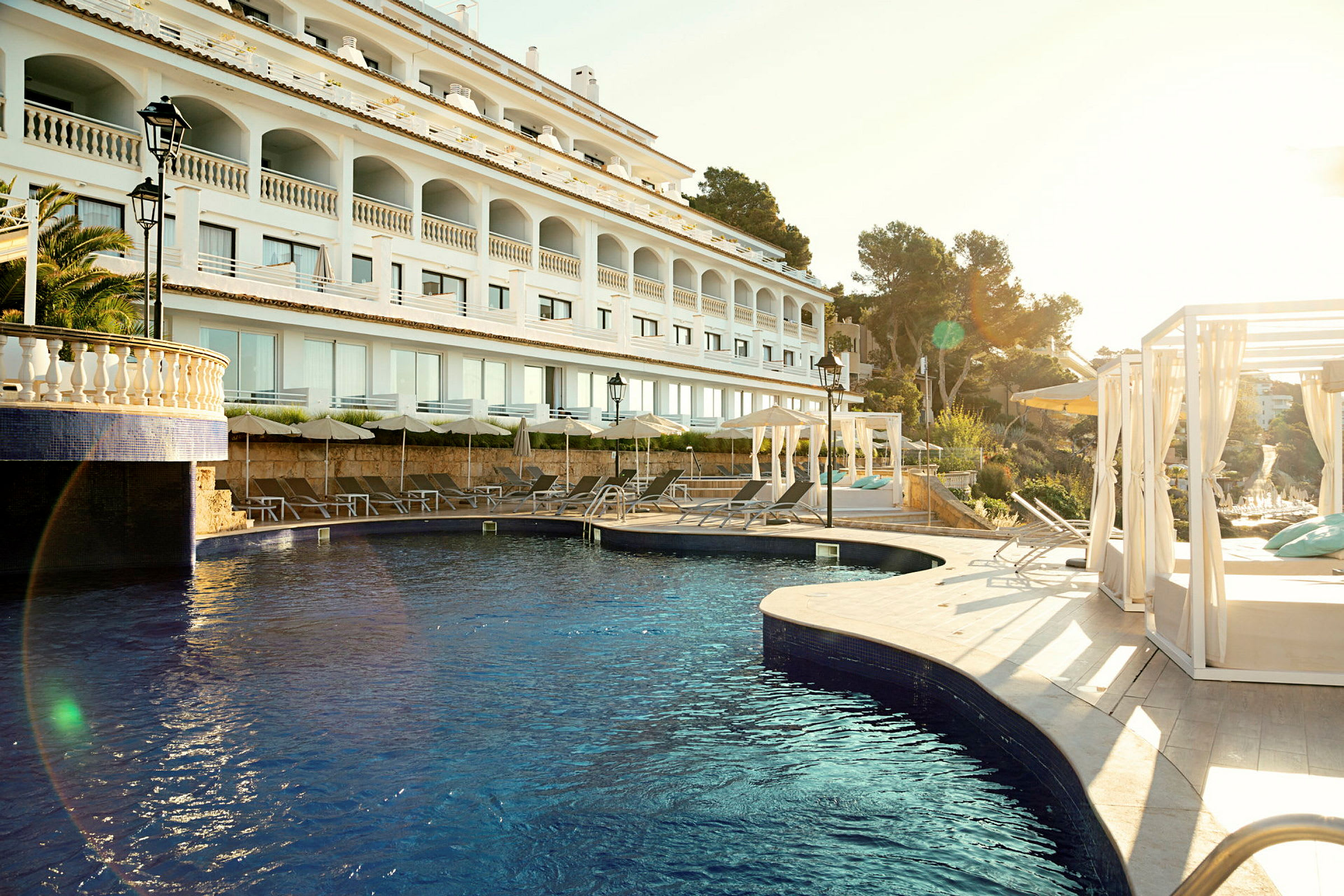 En moderne hotellbygning med et utendørs basseng og solsenger under parasoller. (AI-generert tekst)