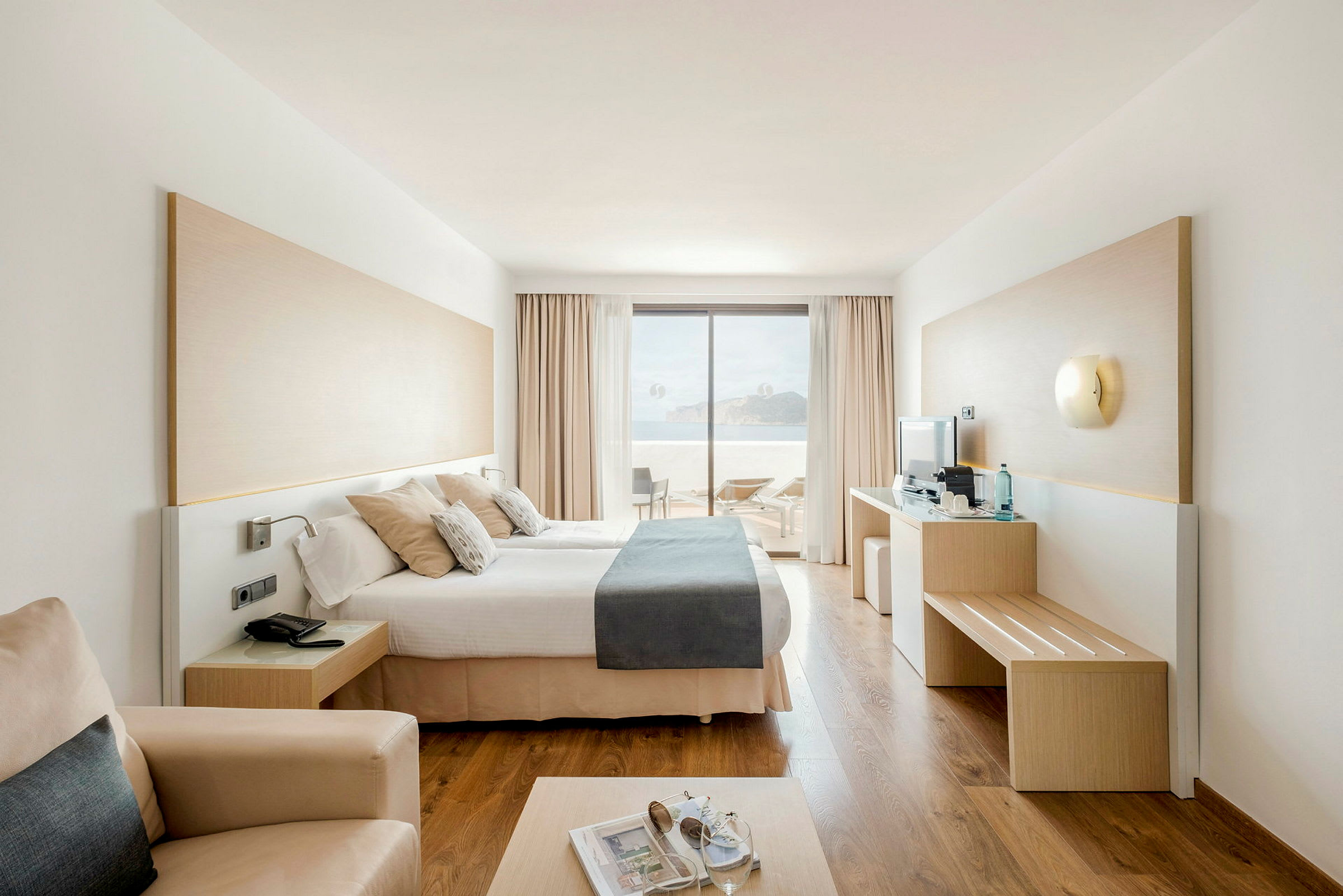 Moderne hotellrom med dobbeltseng og utsikt mot terrasse og hav. (AI-generert tekst)