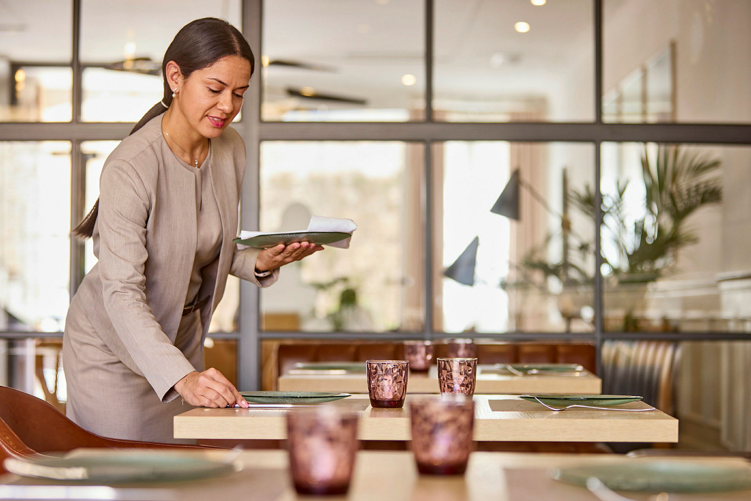 En person ordner tallerkener og glass på et bord i en restaurantmiljø. (AI-generert tekst)