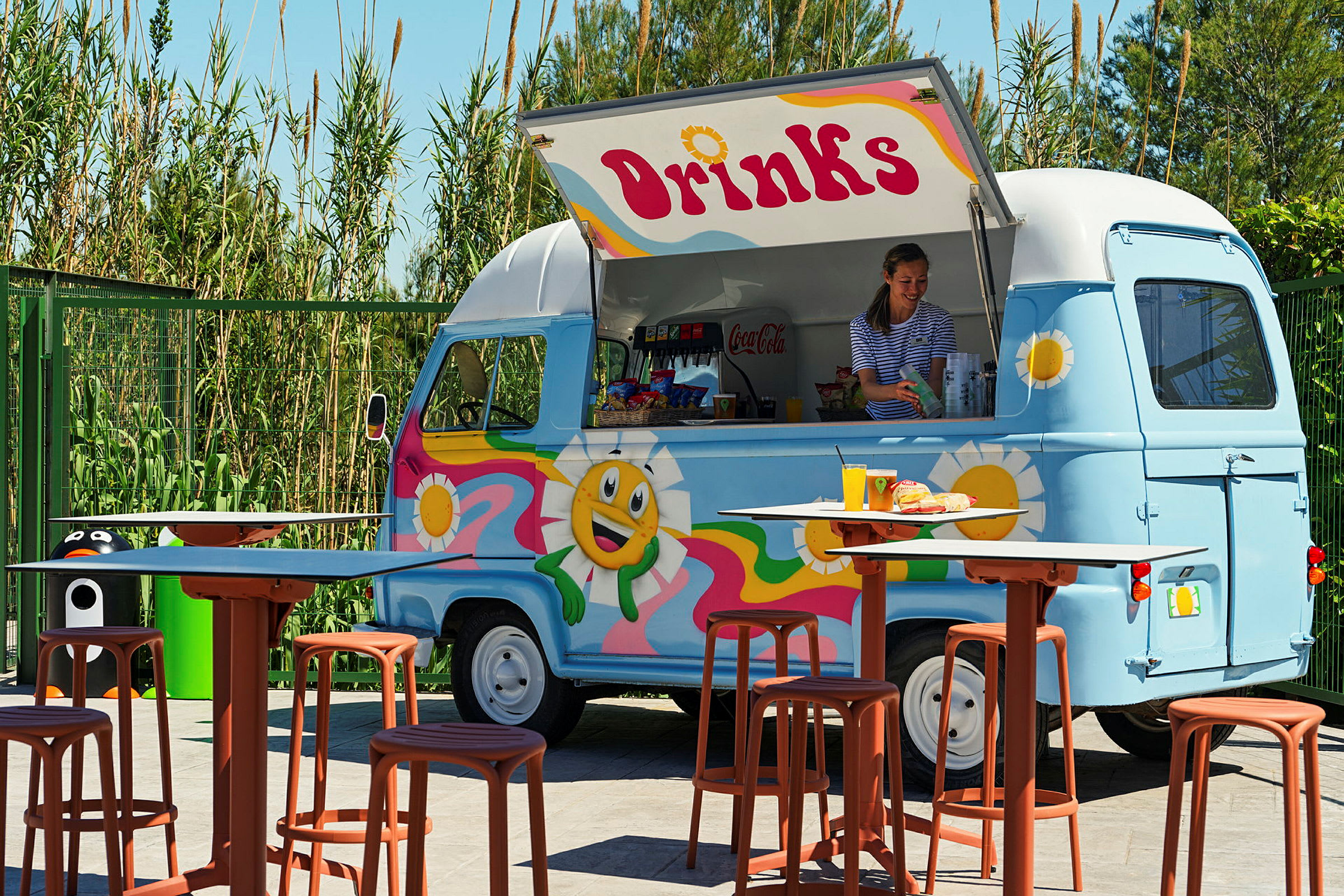En fargerik matbil med teksten 'Drinks' serverer drikker og snacks. Foran bilen står bord og stoler. (AI-generert tekst)