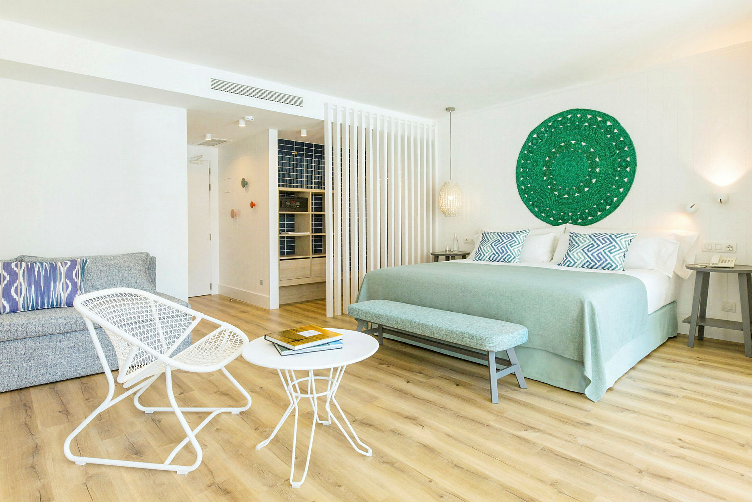 Et lyst hotellrom med en stor seng, to små bord og to stoler, samt en dekorativ veggdekoration. (AI-generert tekst)