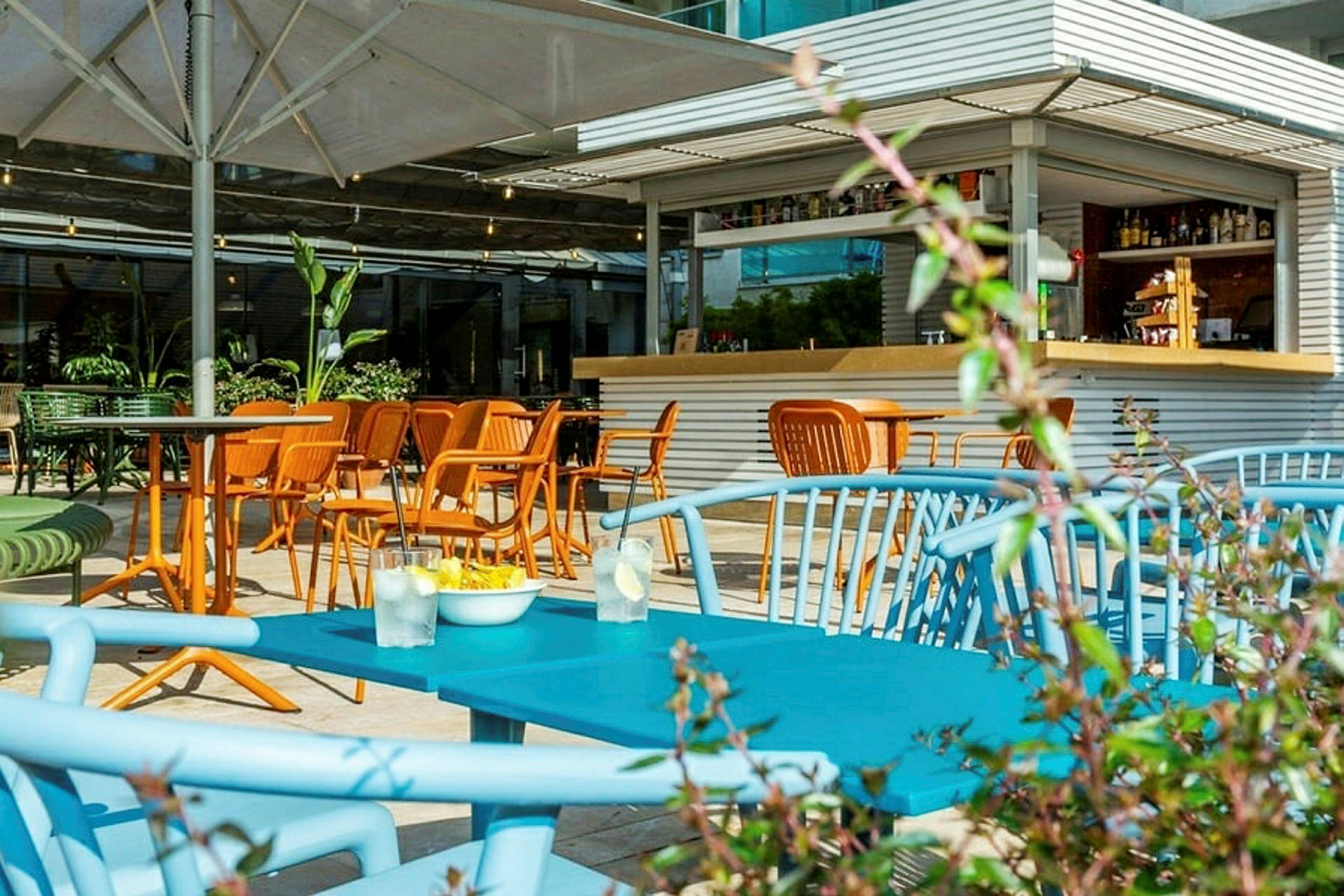 Bilde av en uteservering med fargerike stoler og bord, samt en liten bar i bakgrunnen. (AI-generert tekst)