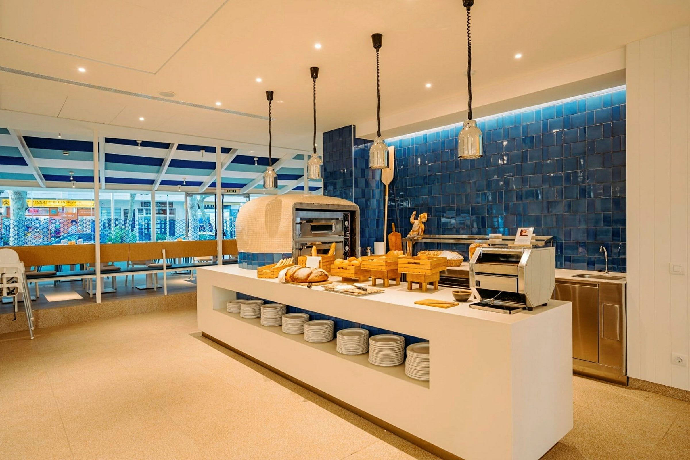 Moderne restaurantmiljø med et åpent kjøkken og spisebord i fokus. Brød og kjøkkenutstyr er plassert på en hvit benk. (AI-generert tekst)