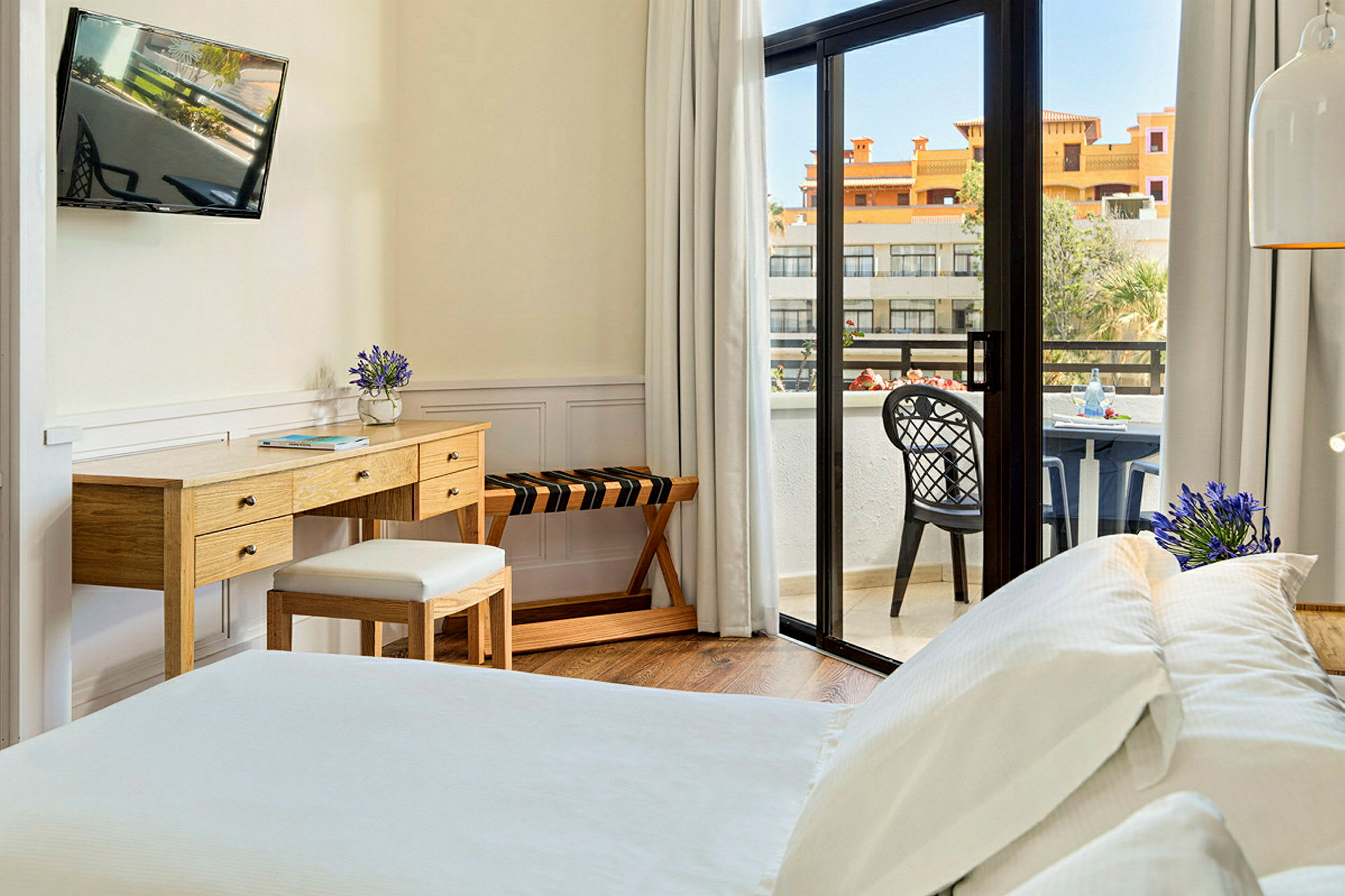 Et hotellrom med en seng, skrivebord og en balkong med utsikt. (AI-generert tekst)
