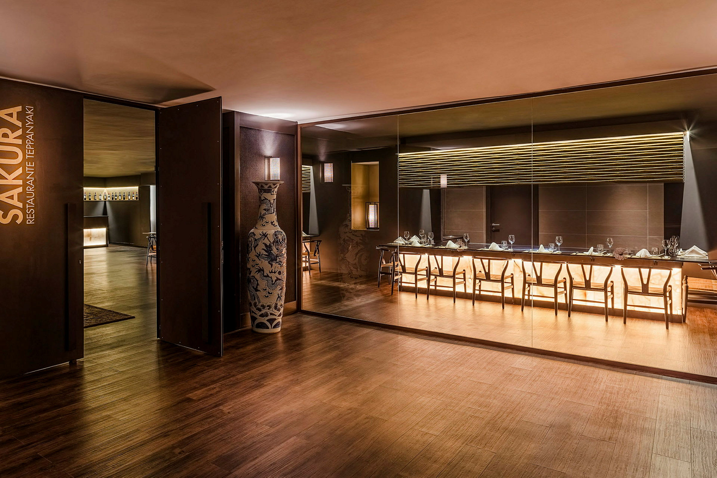 En elegant restaurant med moderne interiør, et stort bord og stoler foran en belyst vegg. (AI-generert tekst)