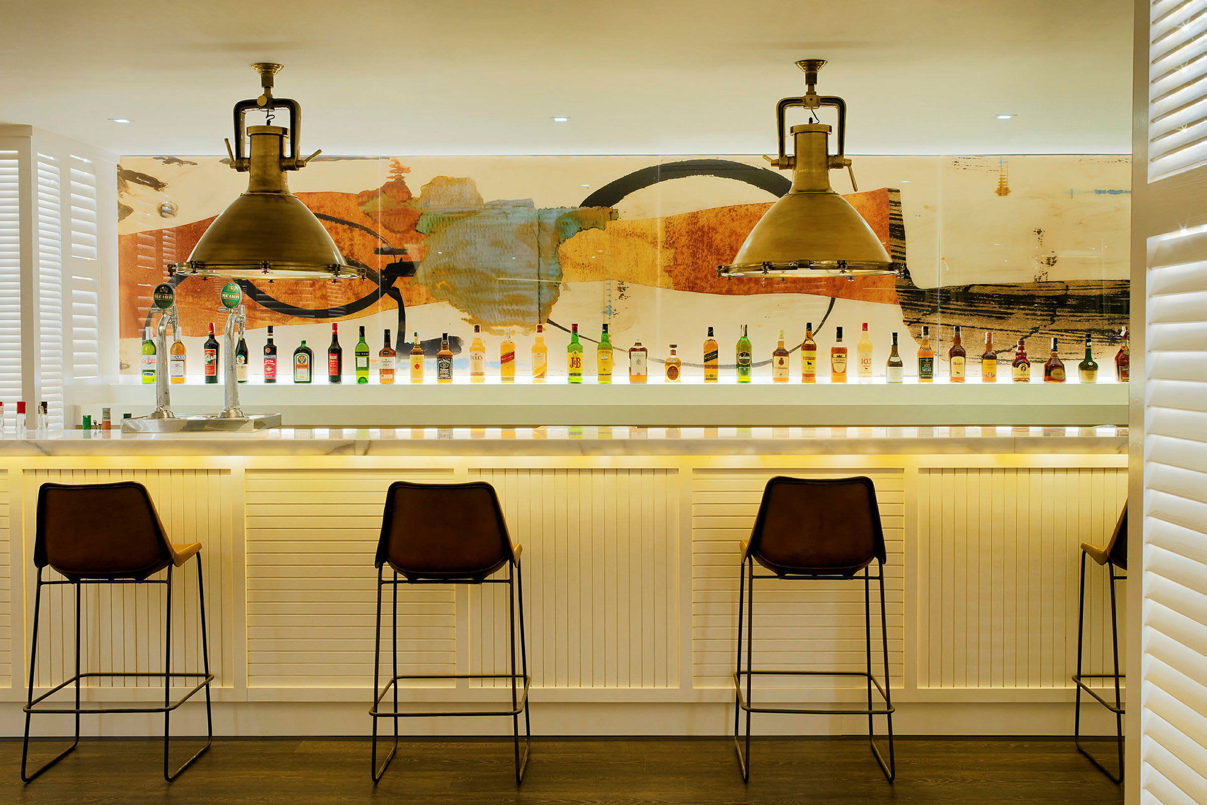 Bilde av en moderne bar med stoler og flasker oppstilt på bardisken foran en fargerik bakgrunn. (AI-generert tekst)