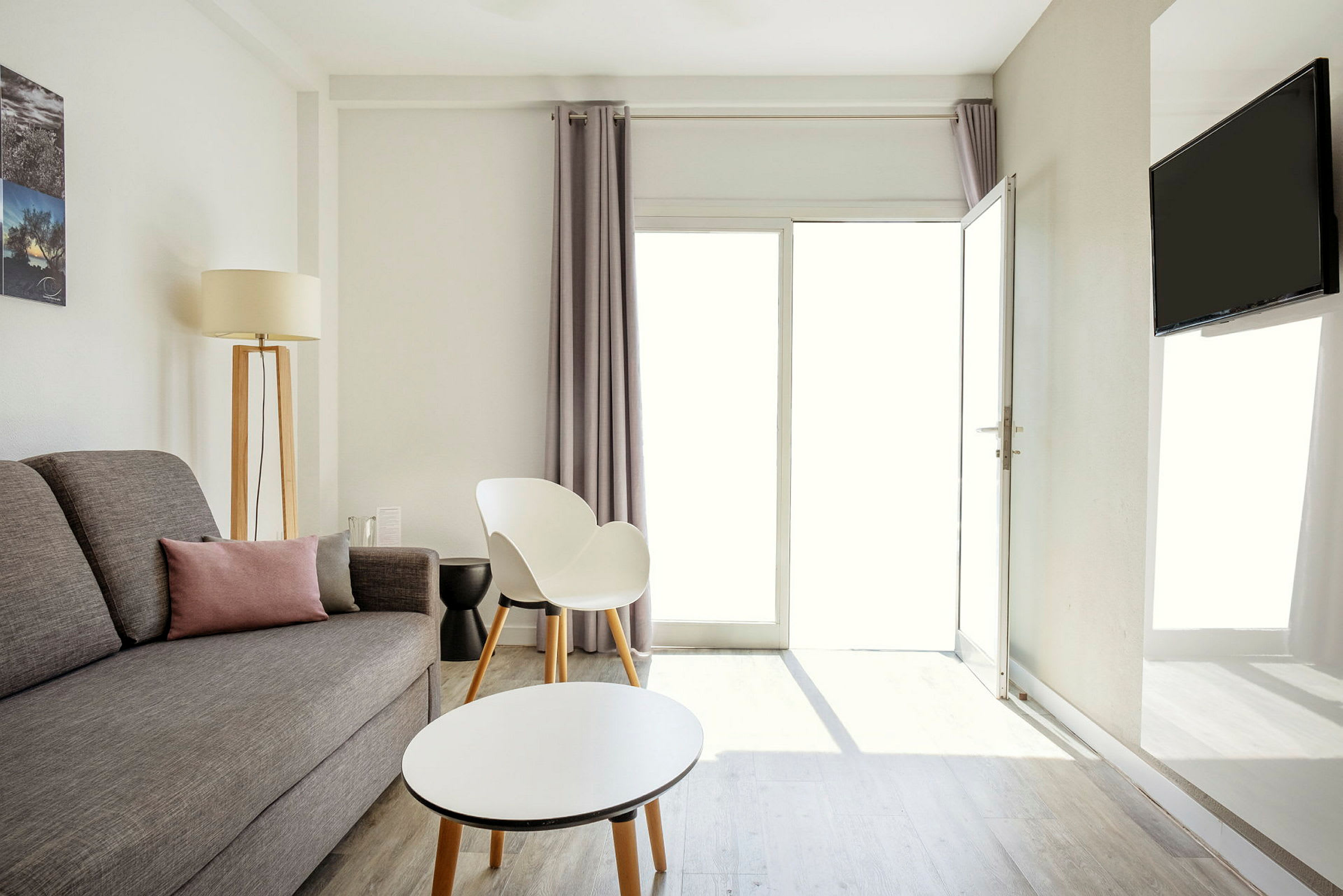 En lys og moderne innredet stue med grå sofa, en hvit stol og et rundt sofabord. (AI-generert tekst)