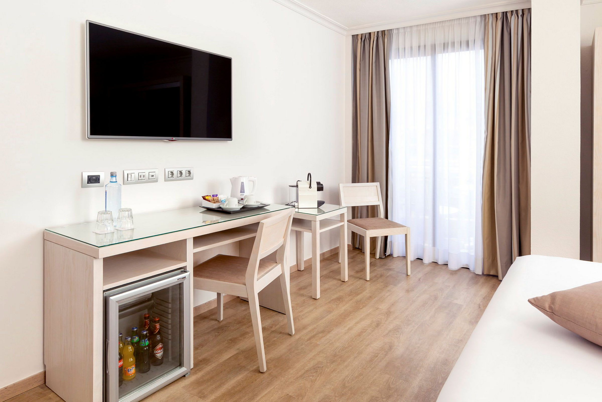 Et hotellrom med skrivebord, stoler, kaffemaskin og minikjøleskap. (AI-generert tekst)