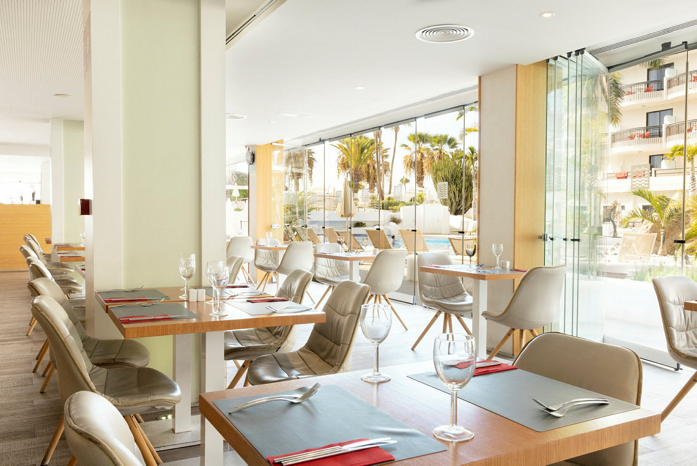 Moderne møblert restaurant med store glassvinduer som vender mot et basseng. (AI-generert tekst)