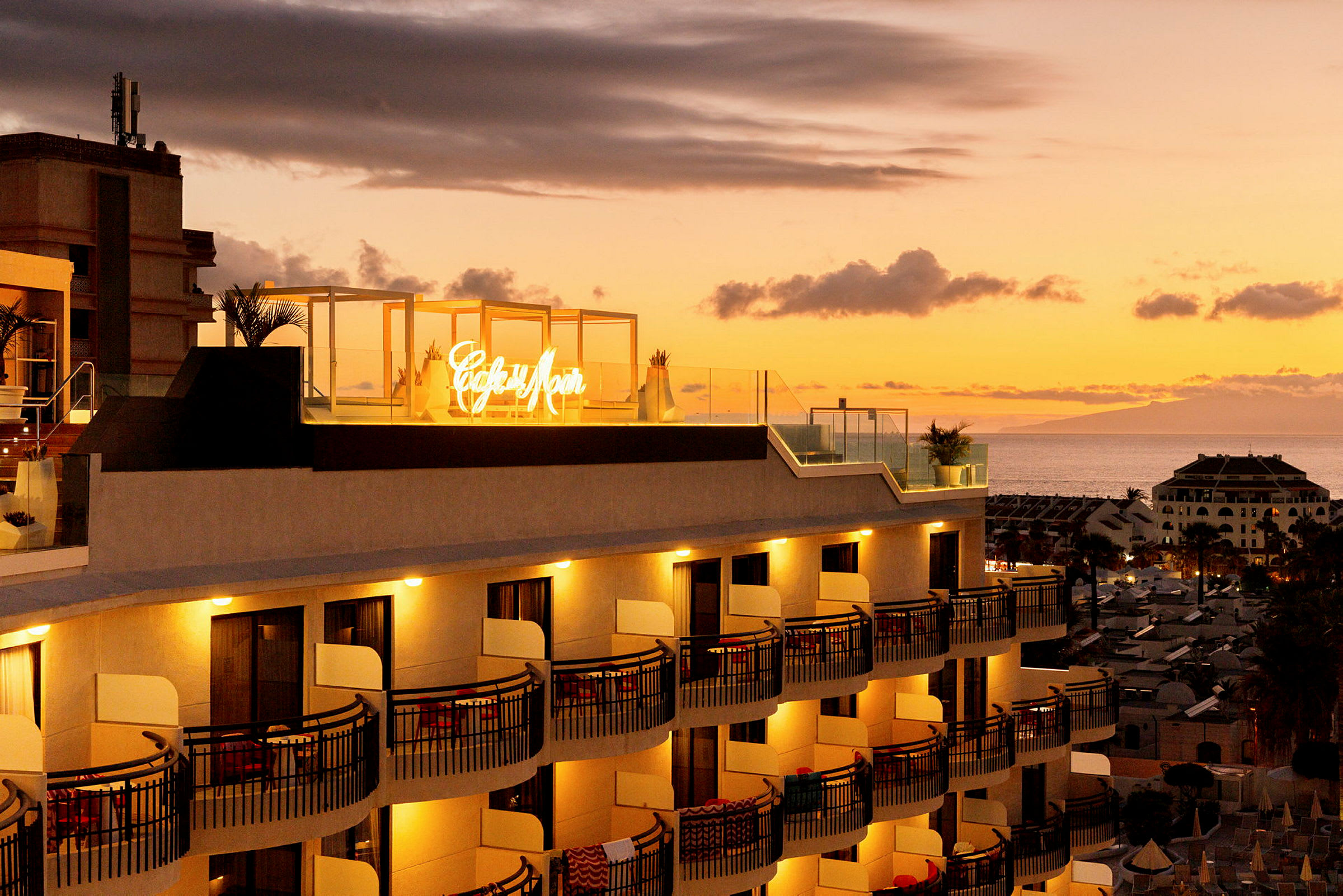 Hotellfasade ved solnedgang med et opplyst skilt på takterrassen. (AI-generert tekst)