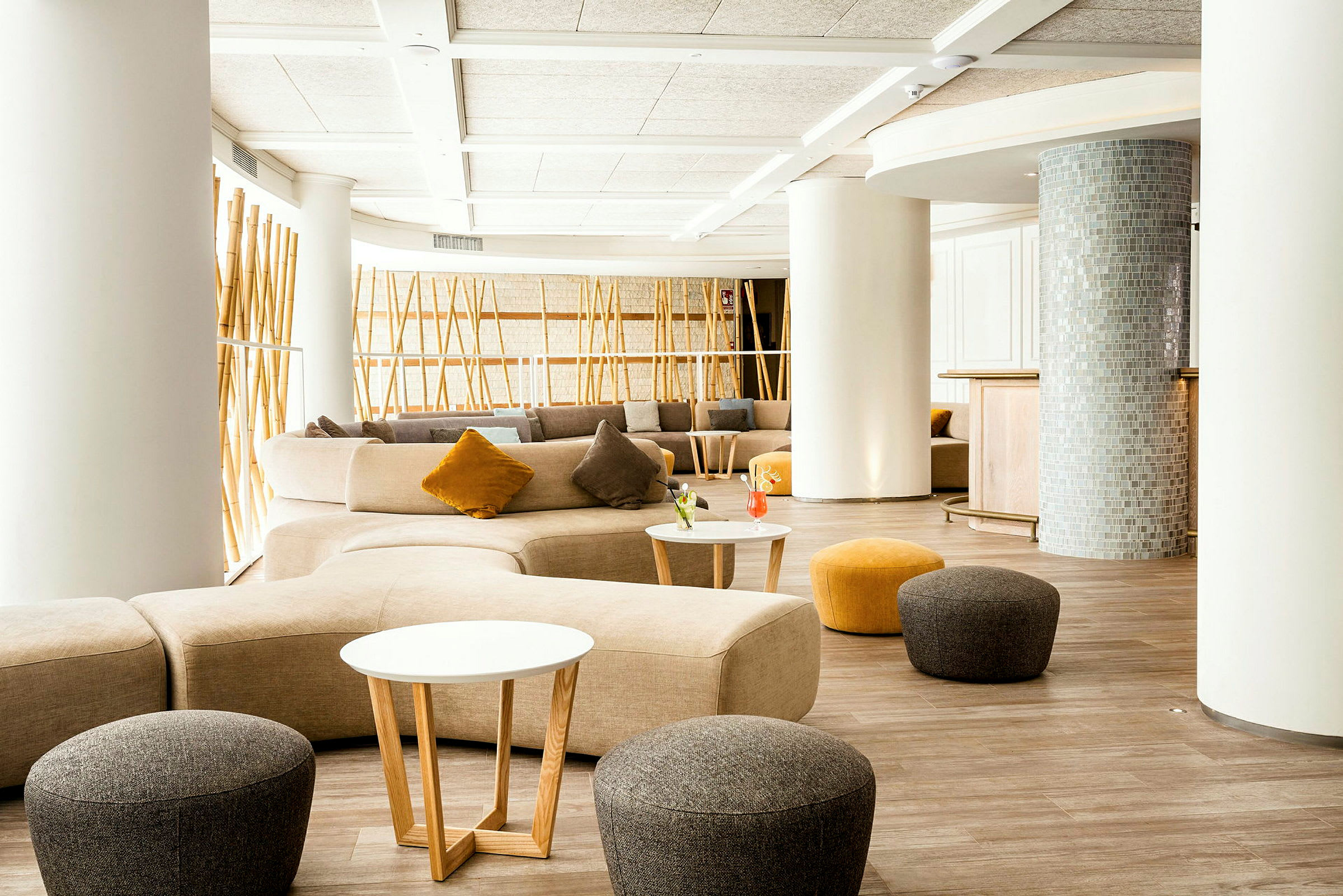 En moderne lounge med lyse møbler, små bord og fargerike puter. (AI-generert tekst)