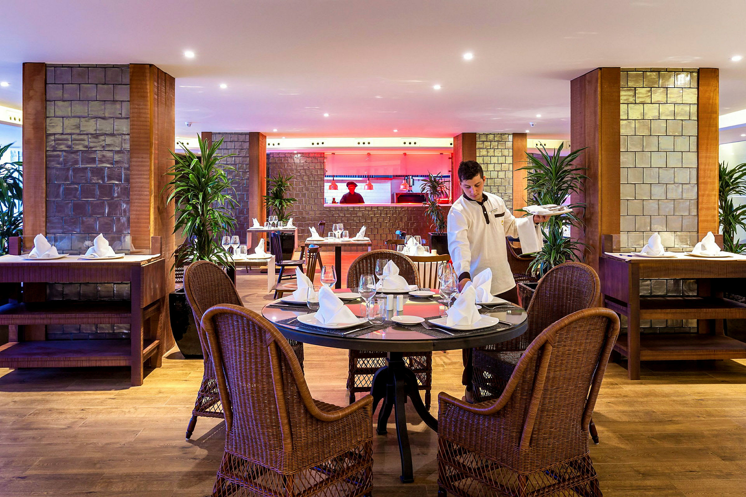 Interiør av en restaurant med rundt oppdekt bord og serveringspersonale. (AI-generert tekst)