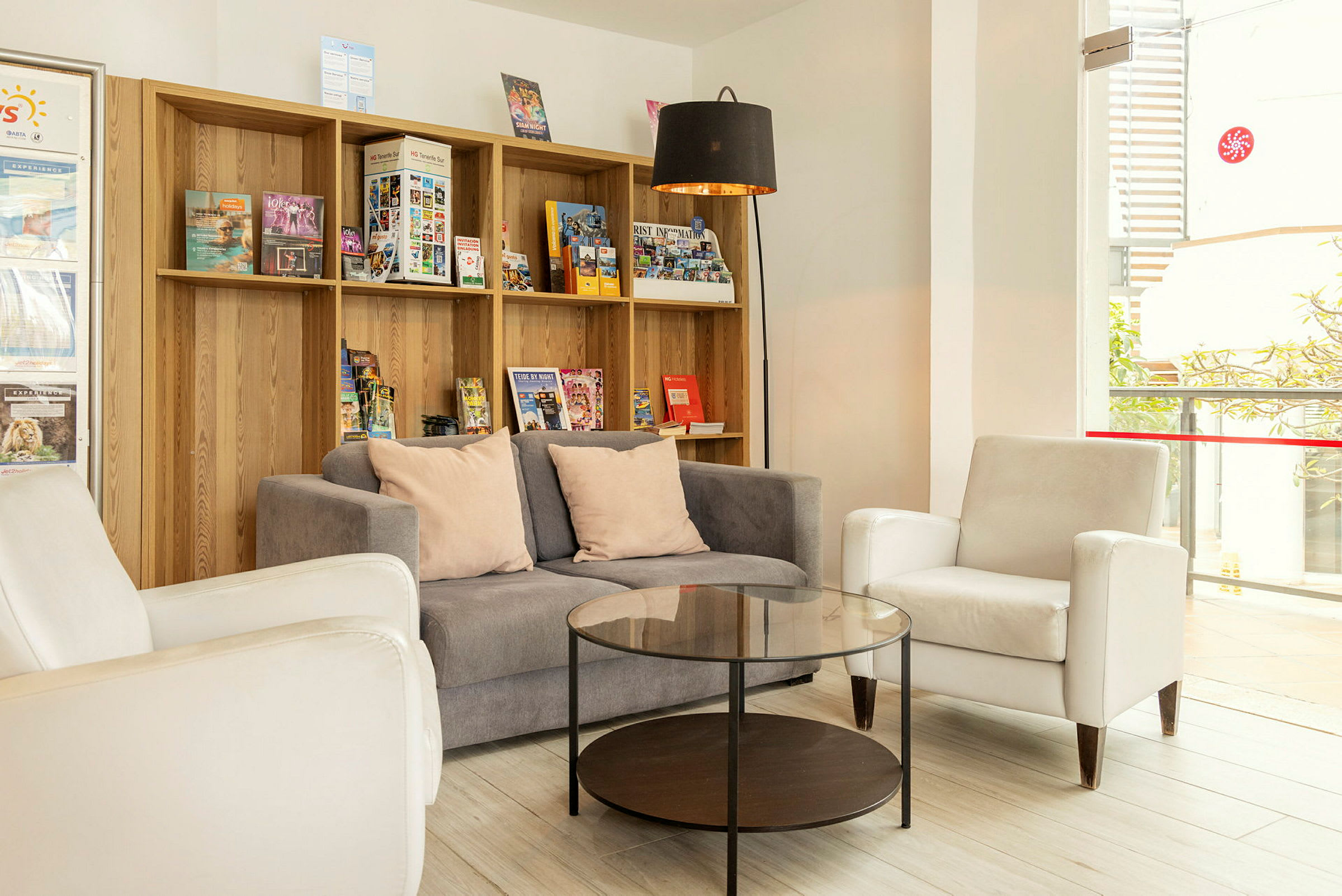 En lounge med sofa, lenestoler og et sofabord foran en hylle fylt med brosjyrer. (AI-generert tekst)