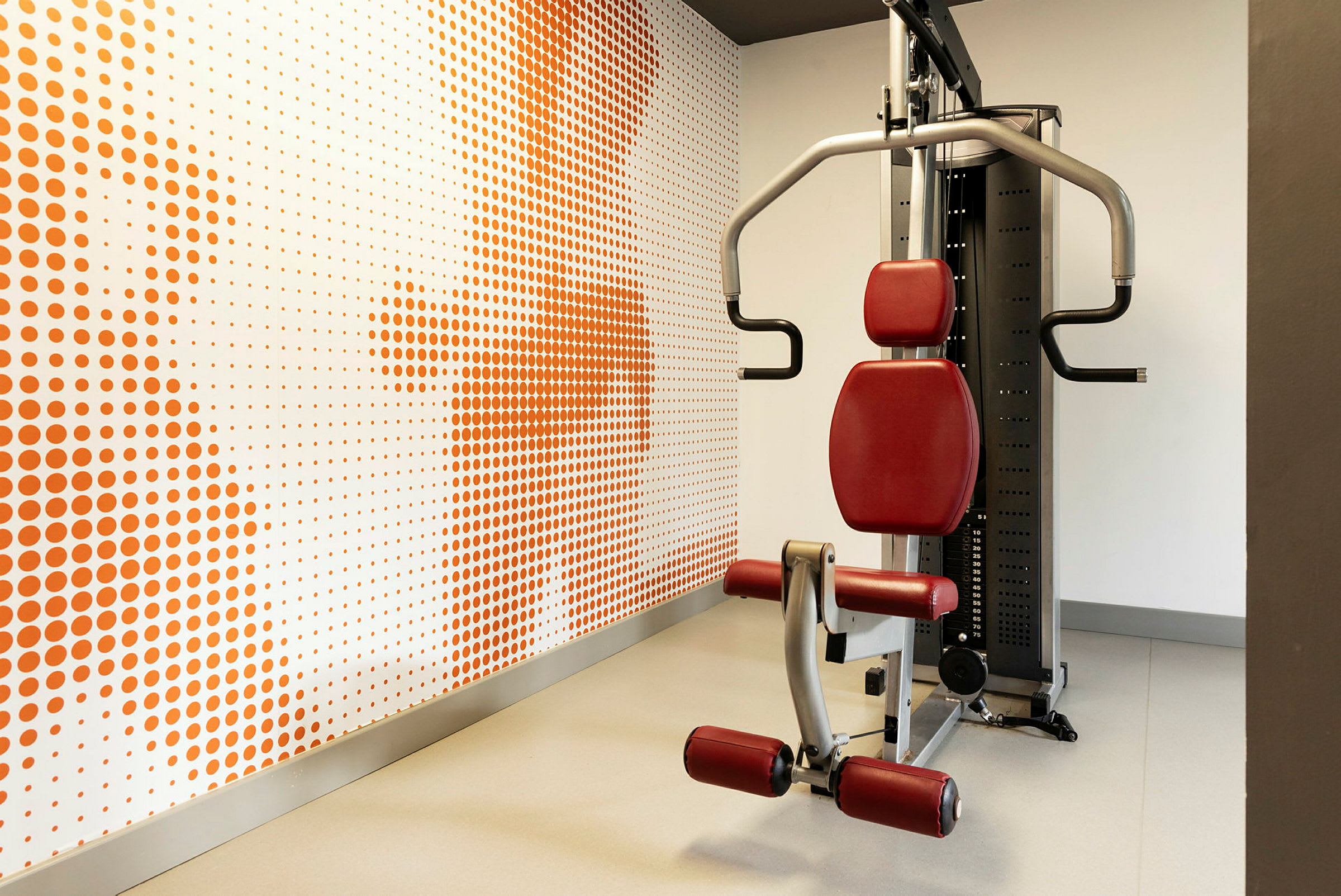 Treningsapparat i et treningsstudio, med en bakgrunn av veggdekor med oransje prikker. (AI-generert tekst)