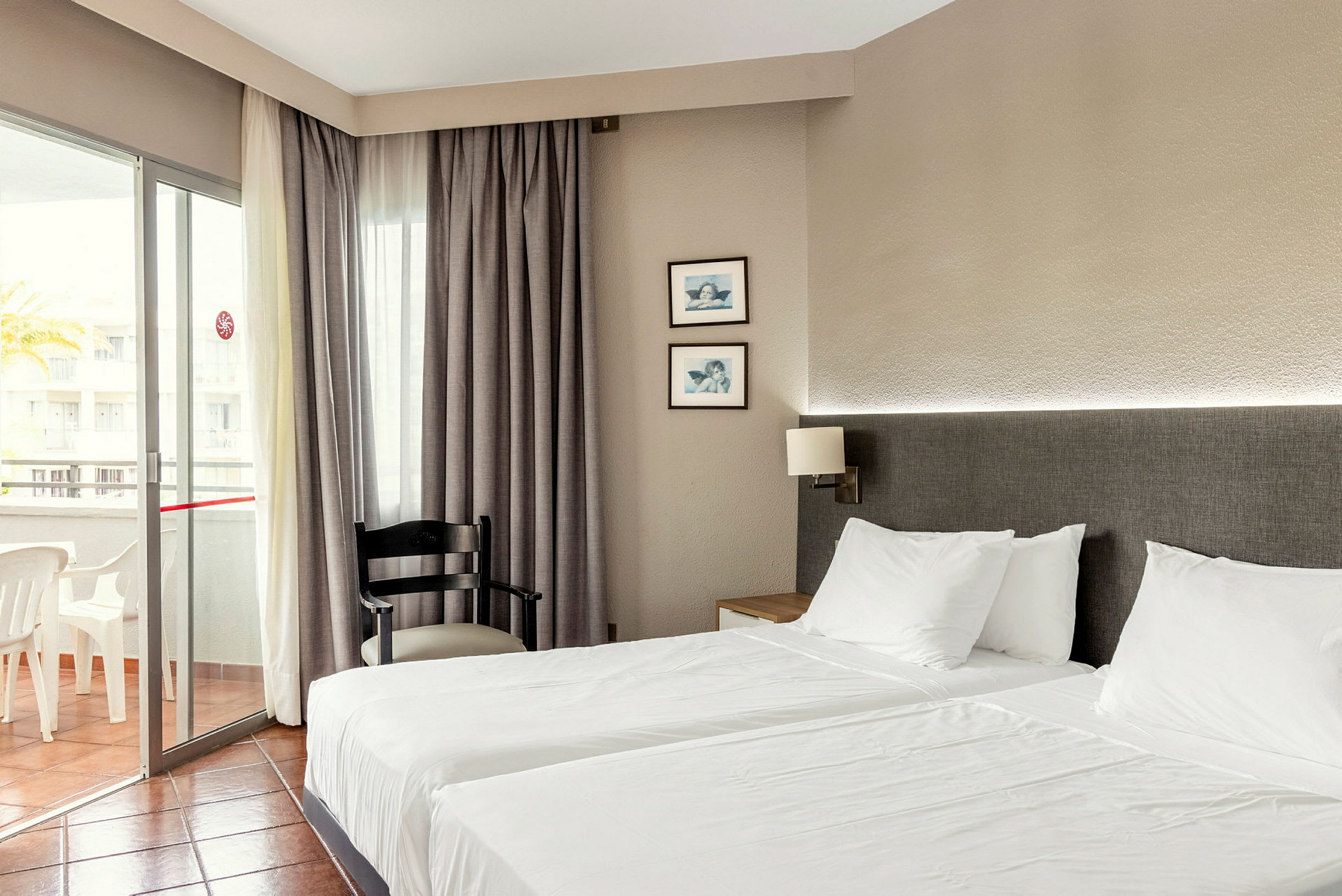 Hotellrom med to enkeltsenger, en stol og en balkong. (AI-generert tekst)