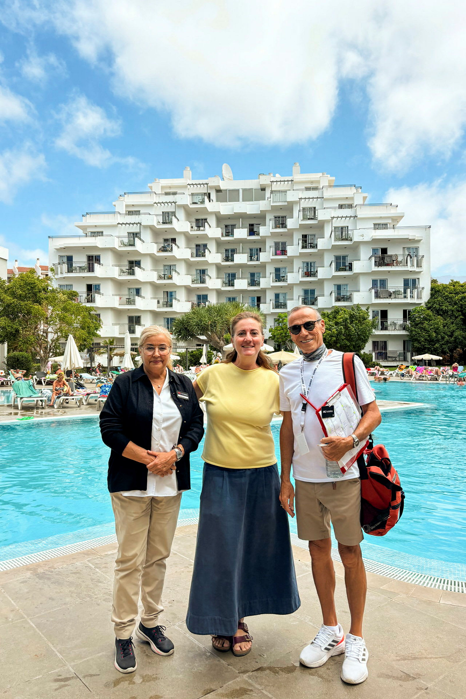 Hotellbygning ved et utendørs basseng med mennesker og solsenger. (AI-generert tekst)