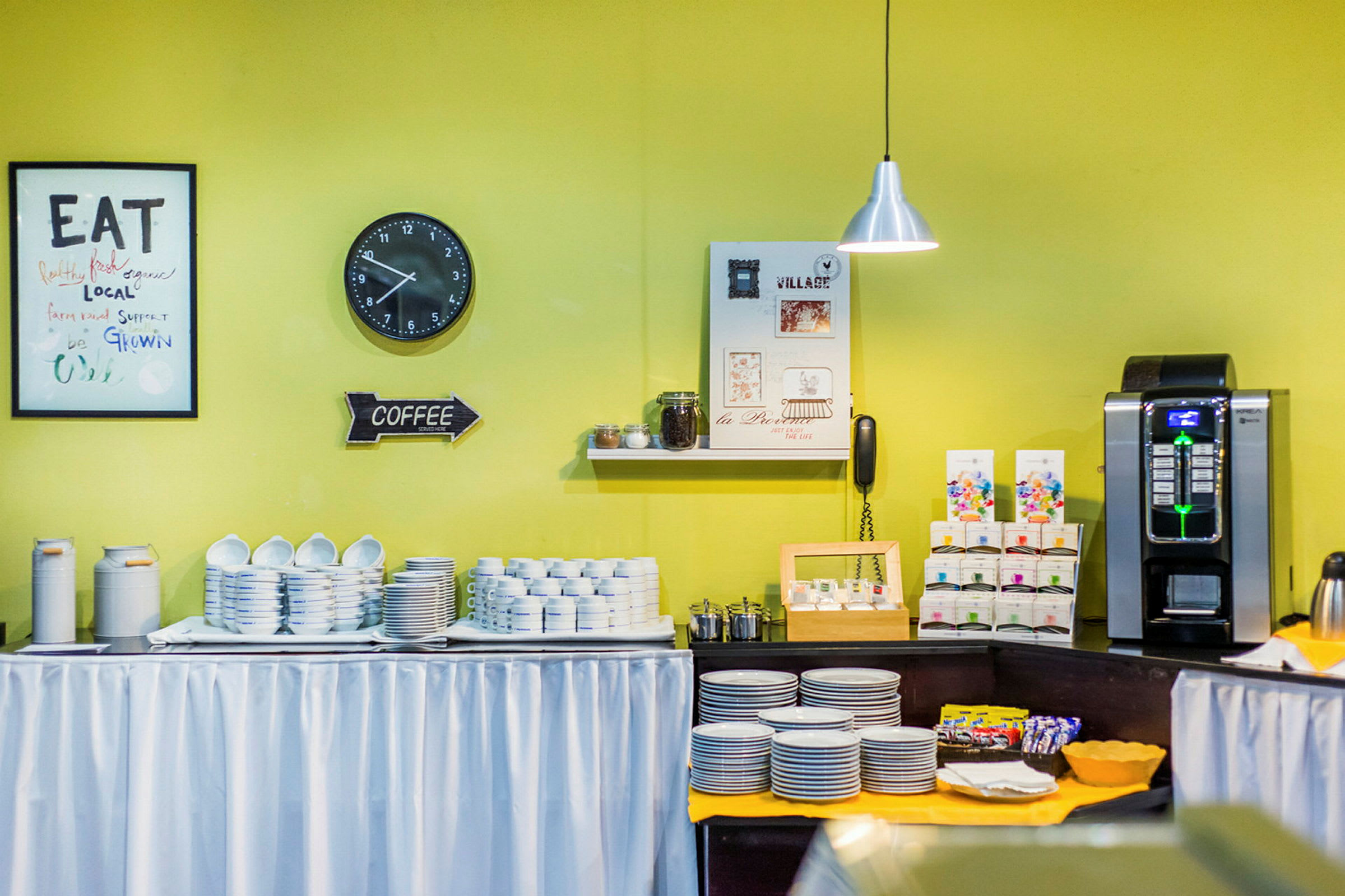 Et bord med servise, en kaffemaskin og diverse tilbehør mot en gul vegg. (AI-generert tekst)